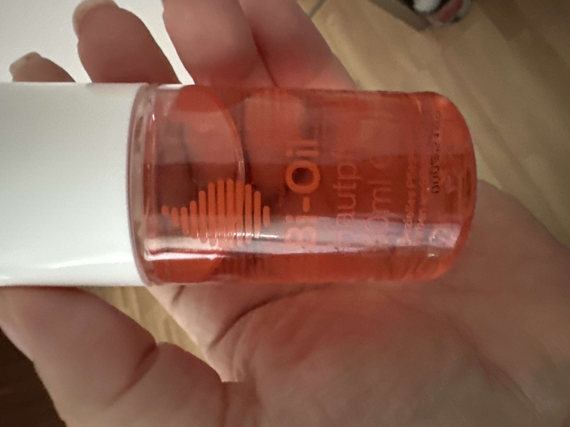The image shows a close-up of a person's hand holding a small, clear, orange-colored bottle. The bottle contains a liquid, and some text is visible on it. The text appears to be in English and possibly another language. Part of the label reads "Bio-Oil" followed by " Beautypflege" and "50ml". There is also a serial number or batch code visible on the bottle that reads "00052149". The background of the image is blurred and appears to be a wooden surface. The lighting suggests it might be indoors, possibly in daylight. The context suggests the photo was taken in Krefeld, Germany.