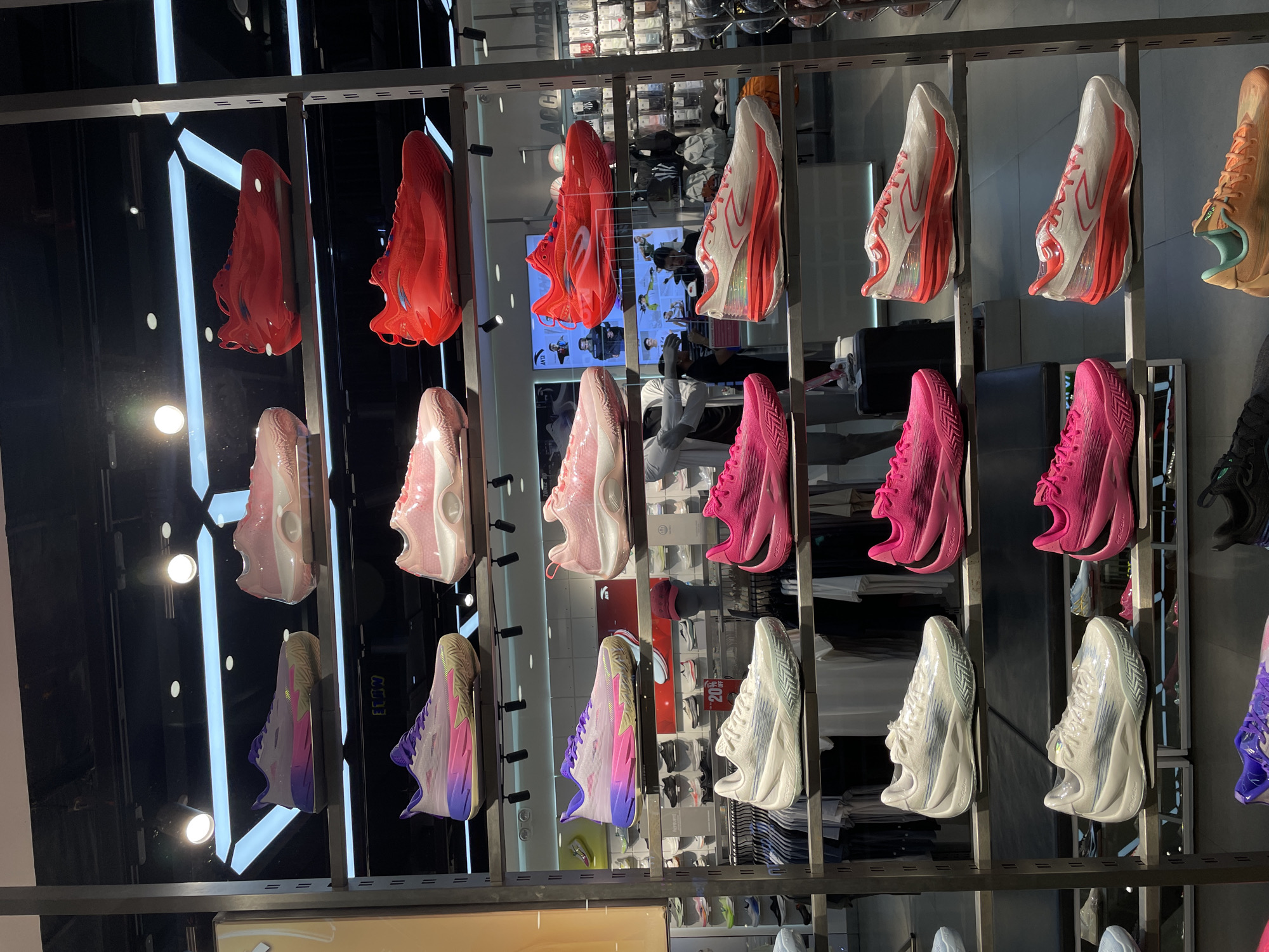 The image shows a retail display of athletic shoes, likely basketball shoes, arranged on multiple shelves within a store. The shoes are primarily in vibrant colors such as pink, red, purple, and white, with some featuring gradient designs. The display is well-lit, highlighting the products. In the background, there are glimpses of other merchandise and store fixtures. The overall environment appears to be a modern sporting goods store. The location is specified as Davao City, Philippines.