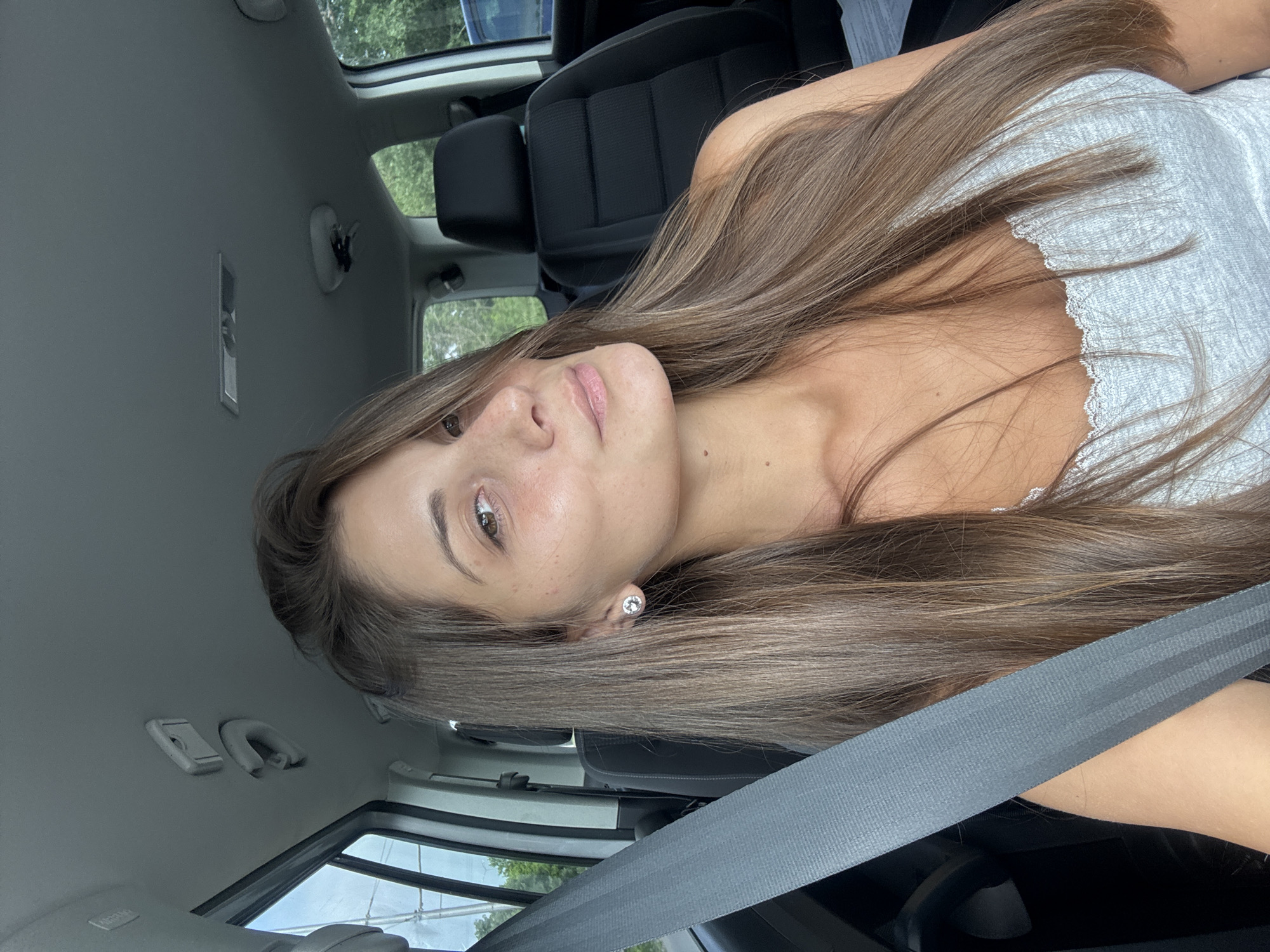 A woman is seated in the driver's seat of a car, wearing a gray shirt and a seatbelt. The car's interior is visible, including the black seat covers and gray ceiling. The location is indeterminable, as there is no Burgas, Bulgaria specific information included in the picture.