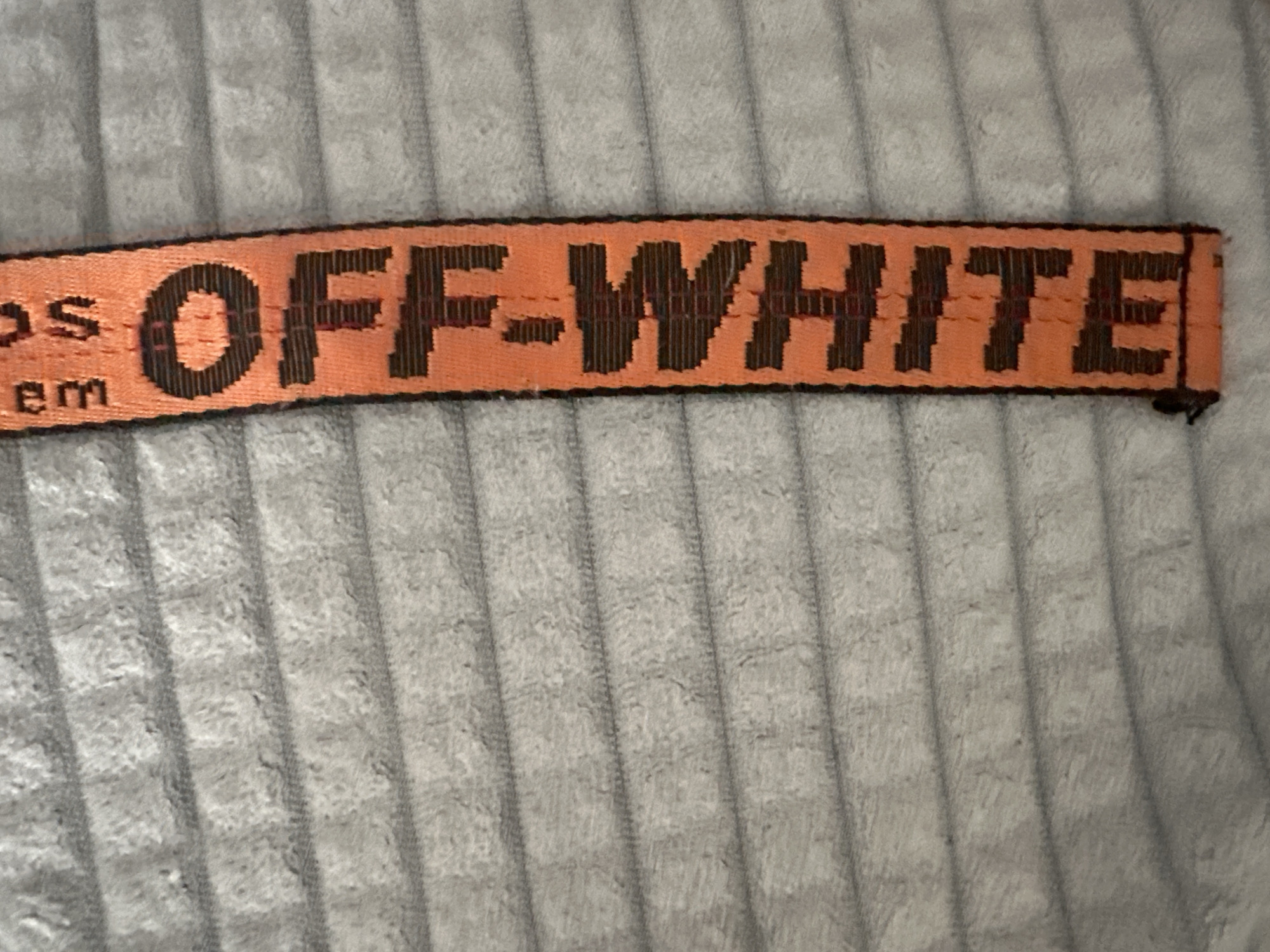 The image shows an orange belt with black lettering that says "OFF-WHITE". The belt is lying on a textured, gray surface. There is no indication of the city of Birobidzhan, Russia, in this image.