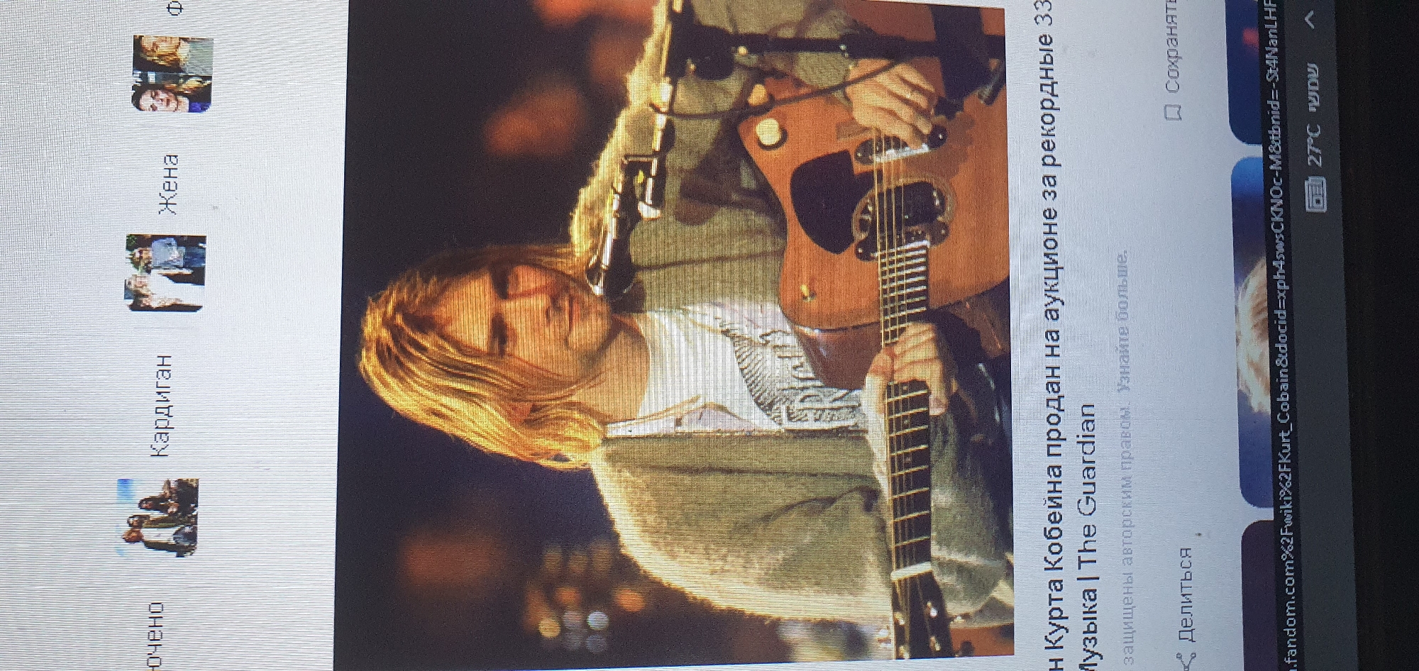 The image shows a screen displaying a web page with a photograph of Kurt Cobain playing an acoustic guitar. He is wearing a light-colored, fuzzy cardigan over a t-shirt. The web page text beneath the image appears to be in Russian and discusses the sale of something belonging to Kurt Cobain at auction. There are also small thumbnail images and text labels in the upper portion of the screen, including "Женa" (Wife) and "Кардиган" (Cardigan). The lower part of the screen shows a web browser's address bar with a URL and the current temperature and time displayed as 27°C and "שמע" (Shema). There is no information in the image that indicates the location is the city of Bat Yam, Israel.