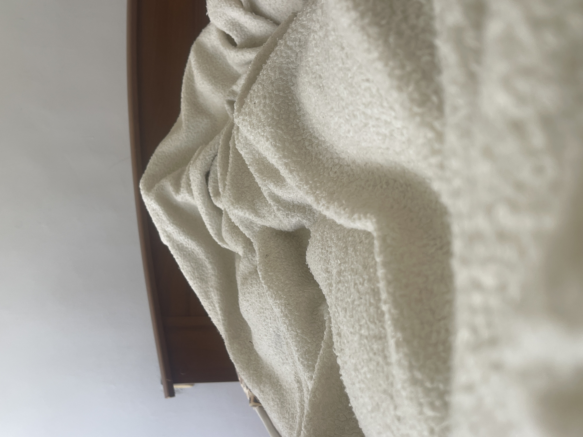 The image shows a close-up view of a rumpled white blanket covering a bed. A wooden headboard is visible behind the blanket, and a plain white wall is in the background. The lighting suggests an indoor environment, possibly a bedroom. There are no people or specific landmarks to indicate a location in Varna, Bulgaria.