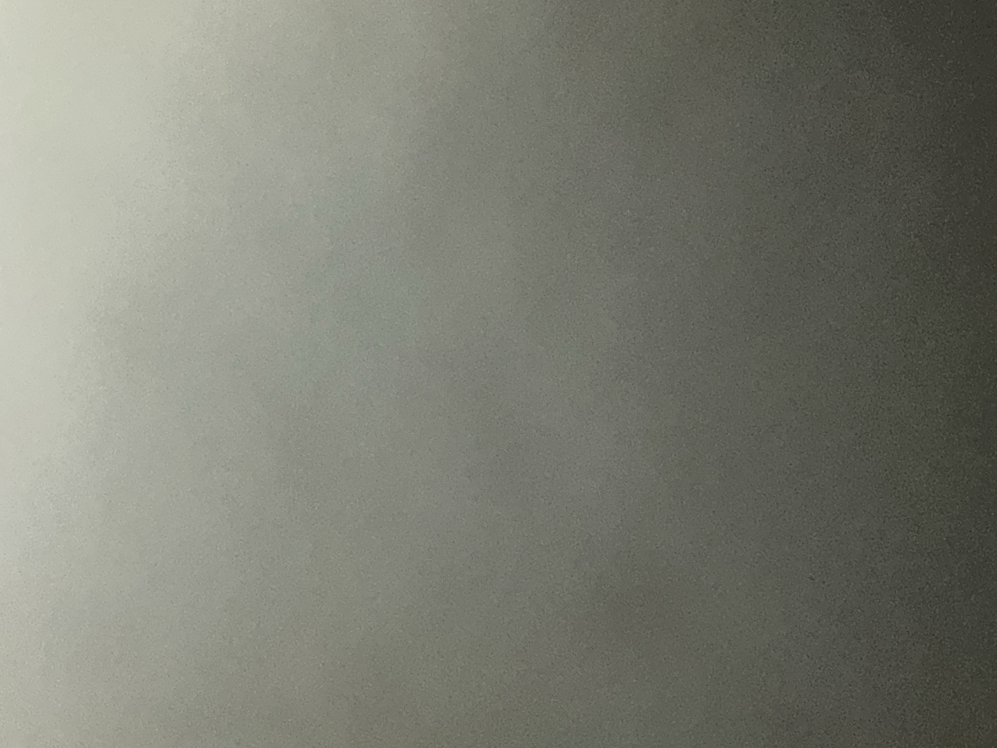 This is a close-up, abstract photograph of a textured surface. The lighting creates a gradient from a bright, almost white, area on the left to a dark, shadowy area on the right. The texture appears grainy or slightly mottled throughout the image. There are no discernible subjects, objects, scenes, activities, or events. No text is visible. The overall impression is one of muted tones and a diffused light source, suggesting an indoor environment or a softly lit outdoor setting. The location context of Belgrade, Serbia, does not provide specific visual cues within this abstract image.