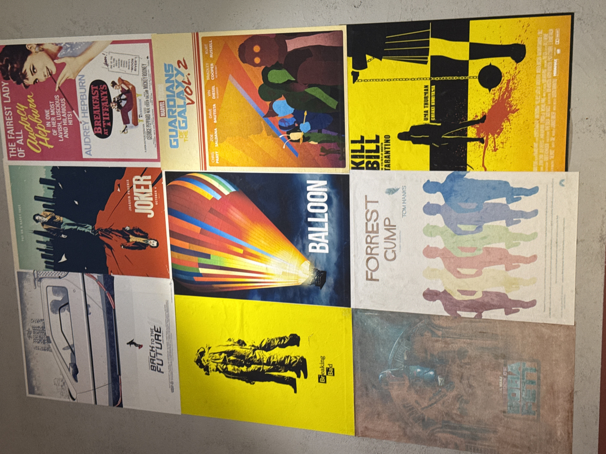 The image shows a collection of movie and television posters arranged on a surface, presumably a floor or wall. The posters include "Breakfast at Tiffany's," "Guardians of the Galaxy Vol. 2," "Kill Bill," "Forrest Gump," "Joker," "Back to the Future," "Breaking Bad," "Balloon," and "Alien." The scene is simple and focuses solely on the posters and the surface they are on. There is no evidence of the city of Saint Petersburg, Russia.