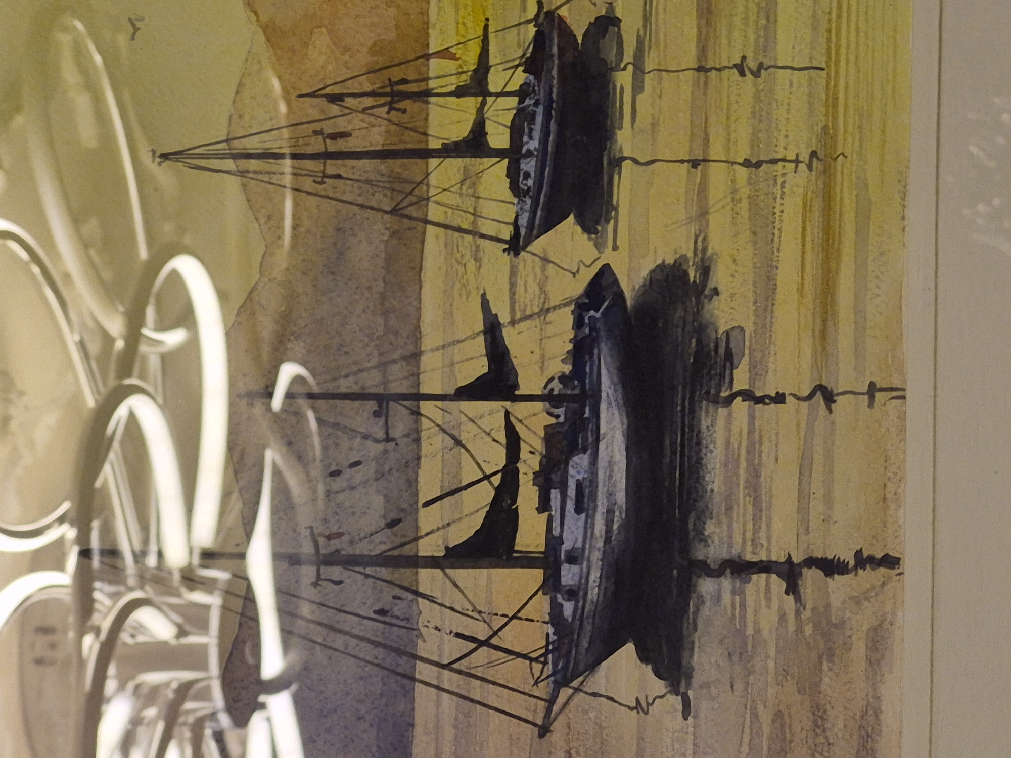 This is a watercolor painting depicting sailboats on water with a mountainous landscape in the background. The painting is framed, and there appears to be a reflection of a modern light fixture in the upper portion of the image, possibly indicating it is displayed indoors or photographed with an overhead light source. The water is rendered with soft, horizontal brushstrokes, creating a reflective surface. The sailboats are depicted with dark sails and hulls, and their reflections are visible below them. The sky is a muted yellow and brown, suggesting either dawn or dusk. The overall mood is calm and serene. The image does not provide any specific details that would place it in the city of Vanadzor, Armenia.