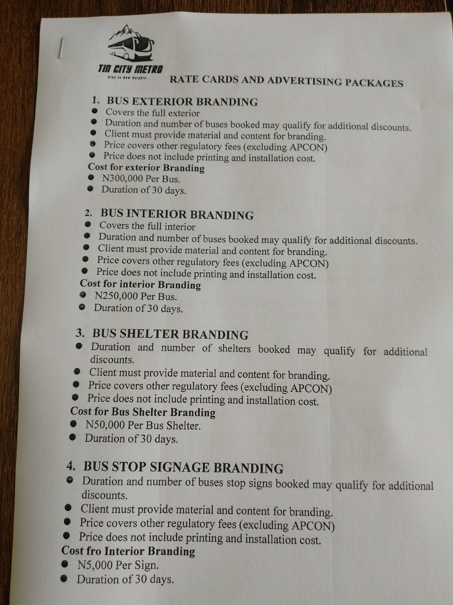 The image is a document containing rate cards and advertising packages for "Tin City Metro" in Barikin Jirga Summa, Nigeria. The document lists four types of branding services: Bus Exterior Branding, Bus Interior Branding, Bus Shelter Branding, and Bus Stop Signage Branding. Each service has a description of what it covers, client requirements, what the price includes and excludes, and the cost per unit with a duration of 30 days. The document appears to be a standard price list or proposal from an advertising company.