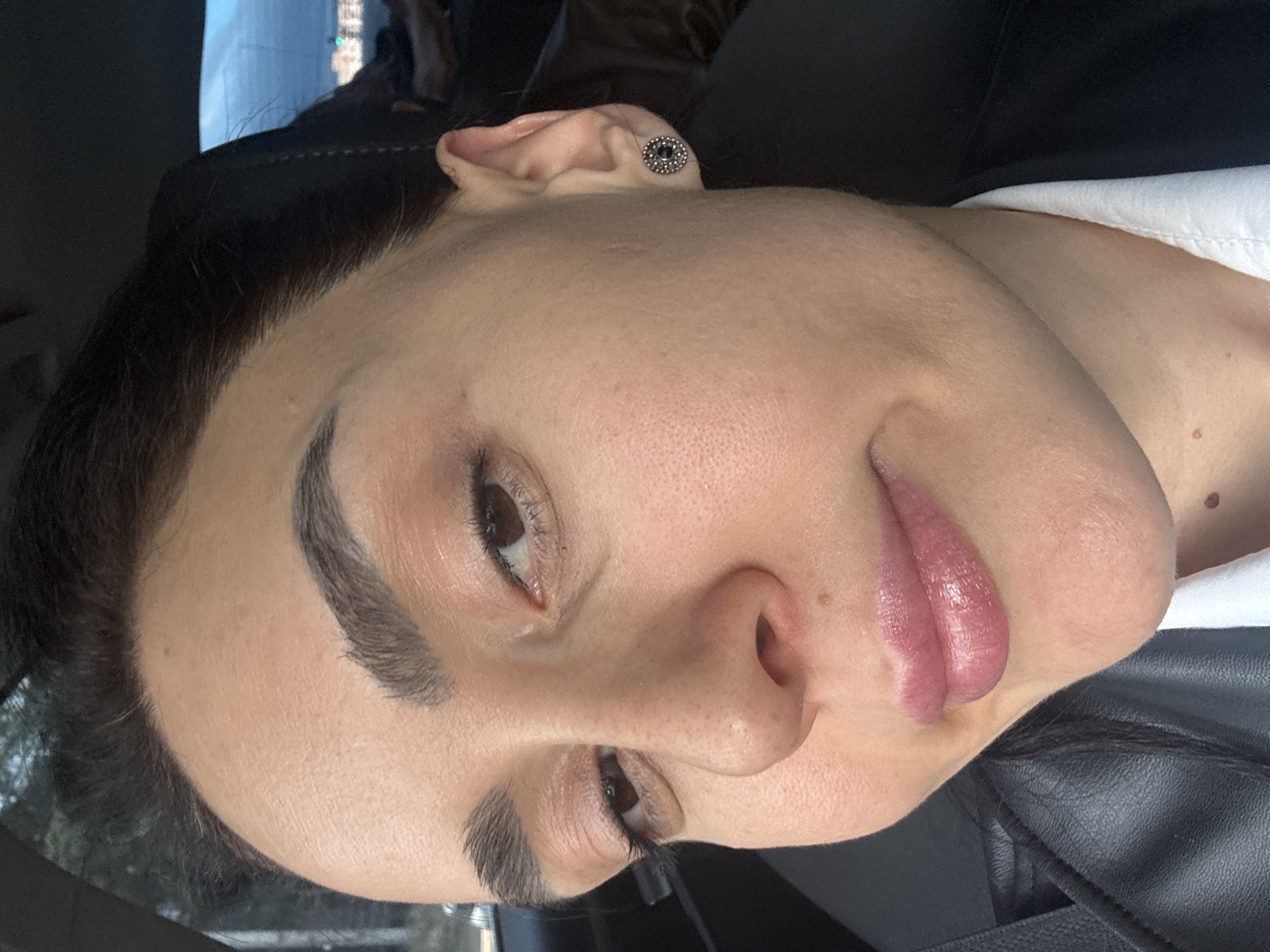 A close-up photograph shows the face of a light-skinned individual with dark hair and makeup, possibly in an indoor setting such as a car. The individual is wearing an earring. The location is not determined from the image.
