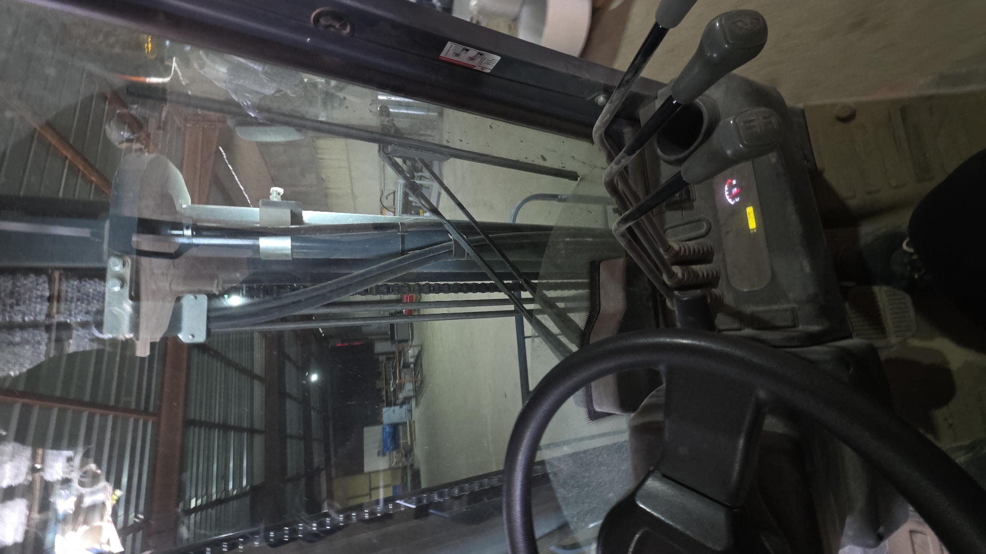 The image shows the interior of a forklift, specifically the driver's cabin, from the driver's perspective. The steering wheel, gear levers, and instrument panel are visible in the foreground. Through the windshield, a warehouse or industrial setting is visible with metal structures and equipment. It is impossible to confirm the location in Balgarevo, Bulgaria, without further evidence.