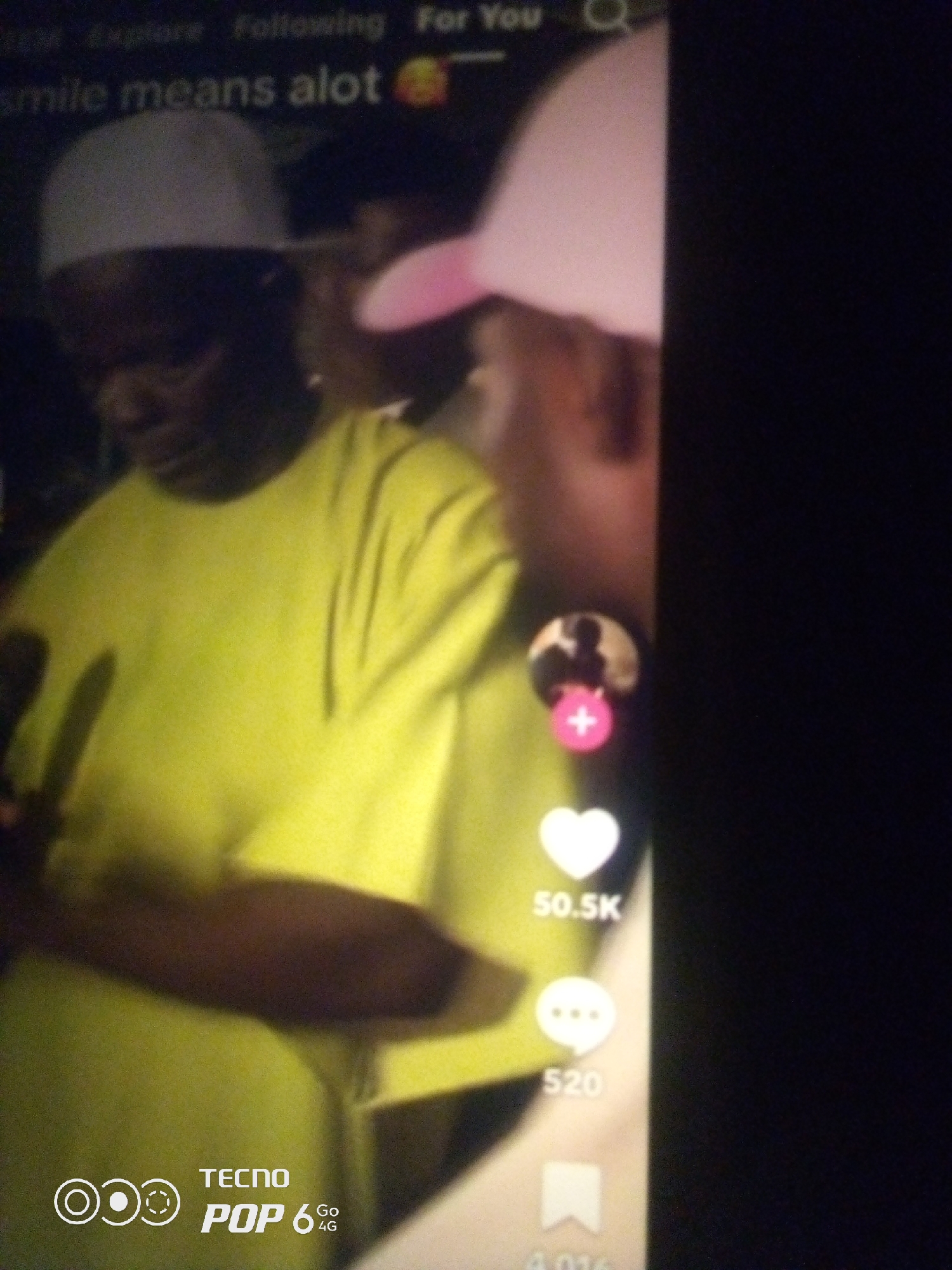 The image shows a TikTok video interface with two individuals visible. On the left, a person wearing a light-colored cap and a bright yellow t-shirt is partially visible, facing away from the camera. To the right, another individual is also partially visible, wearing a pink cap. The TikTok interface elements include a profile picture with a pink plus sign, a white heart icon indicating likes with the number "50.5K" below it, a speech bubble icon for comments with the number "520" below it, and a bookmark icon. Text at the top of the screen reads "smile means alot". The bottom left corner displays the "TECNO POP 6 4G" logo. The scene appears to be indoors, possibly in a home or a public gathering space. There is no information in the image to suggest a location in Howayi, Nigeria.