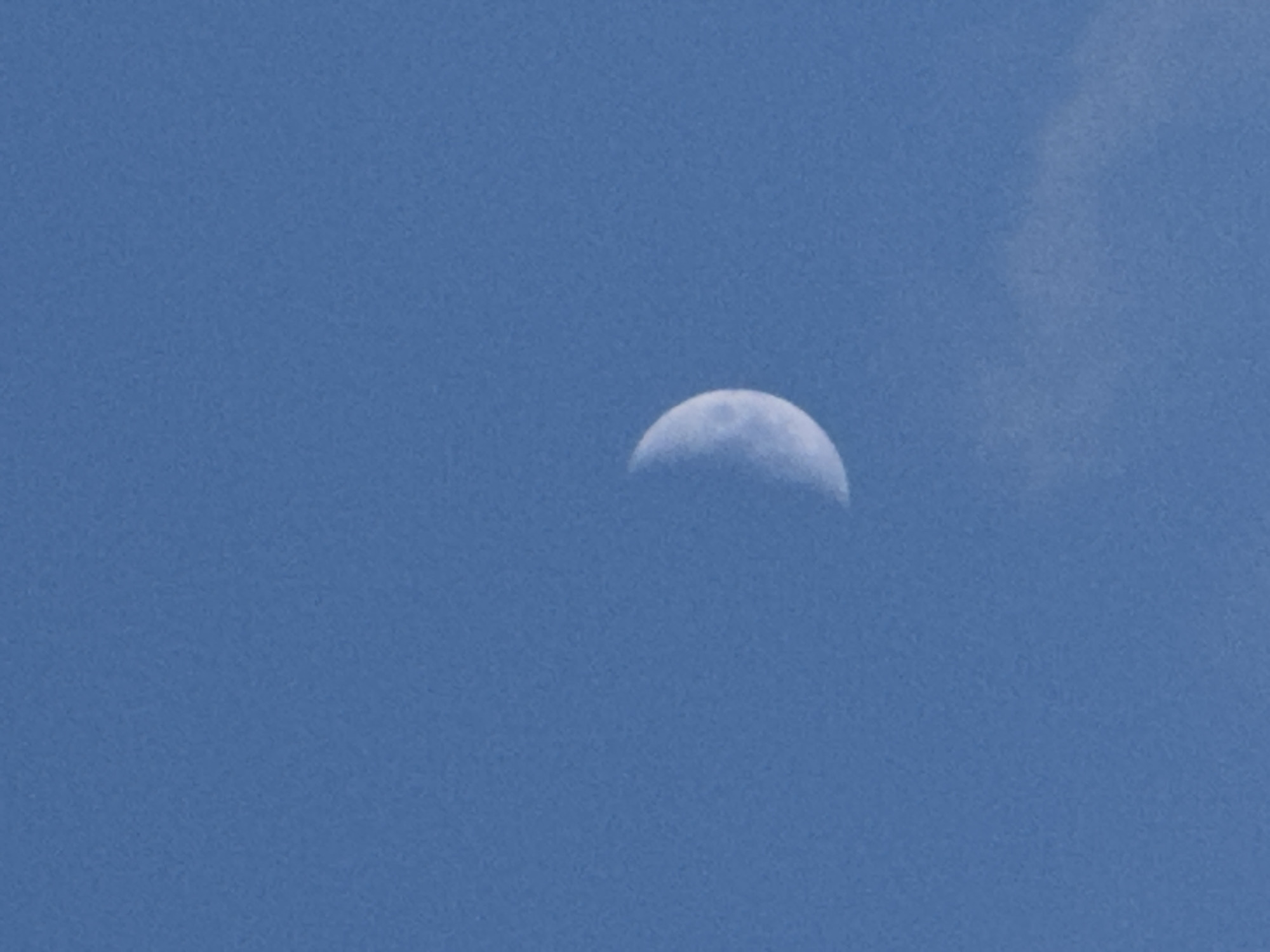 A crescent moon is visible in a clear blue sky, slightly to the left of the center of the frame. A wispy cloud is present in the lower right portion of the image. The image does not contain any elements that would allow for identification of its location in Chaikovsky, Russia.