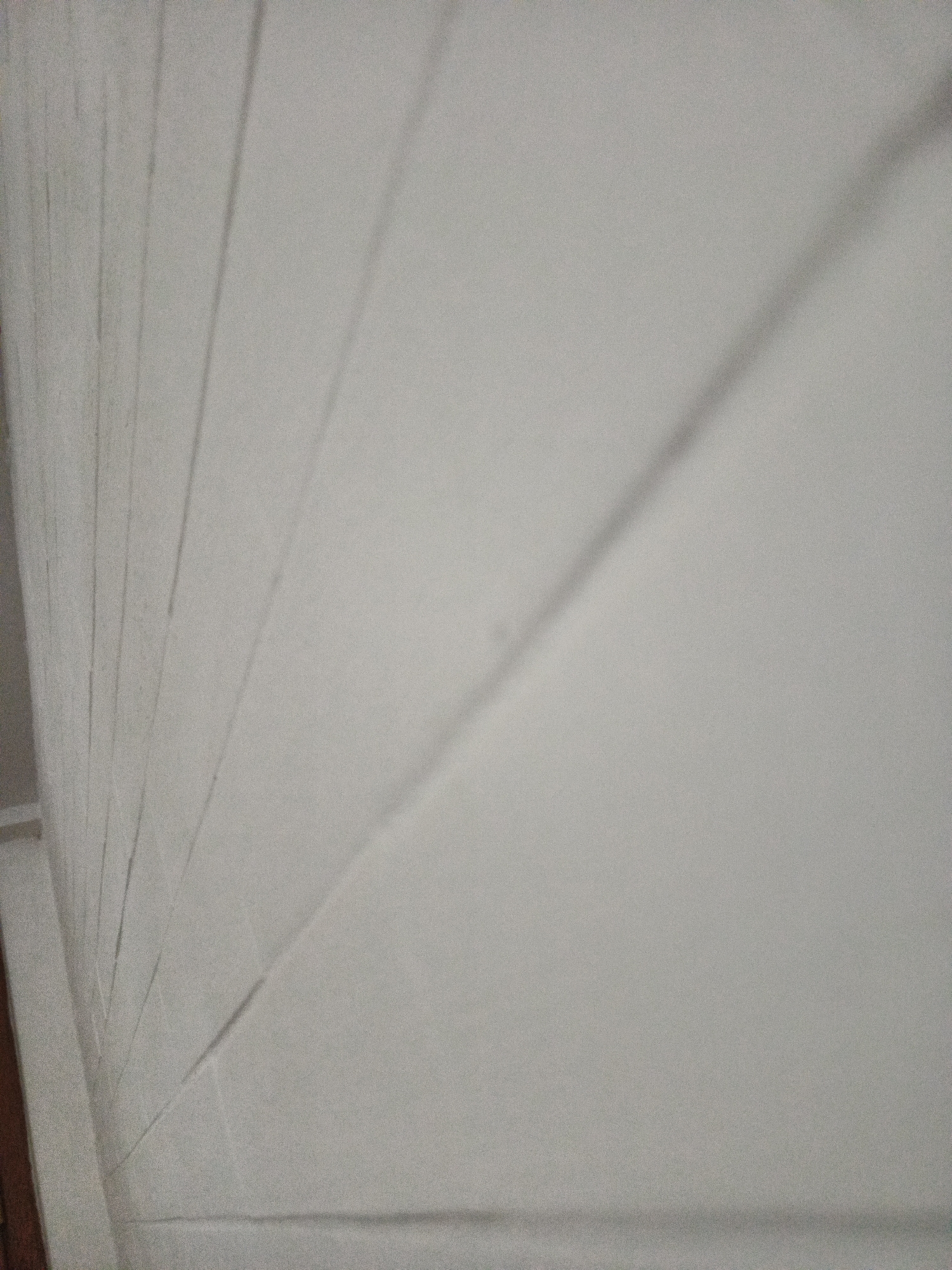 I cannot provide a location for the image, but I can describe the image. The image shows a white wall with vertical lines and shadows. It appears to be a close-up shot of a textured wall or a wall with paneling. There is a door frame visible on the left-hand side of the image. The angle of the shot is tilted, giving a perspective view of the wall.