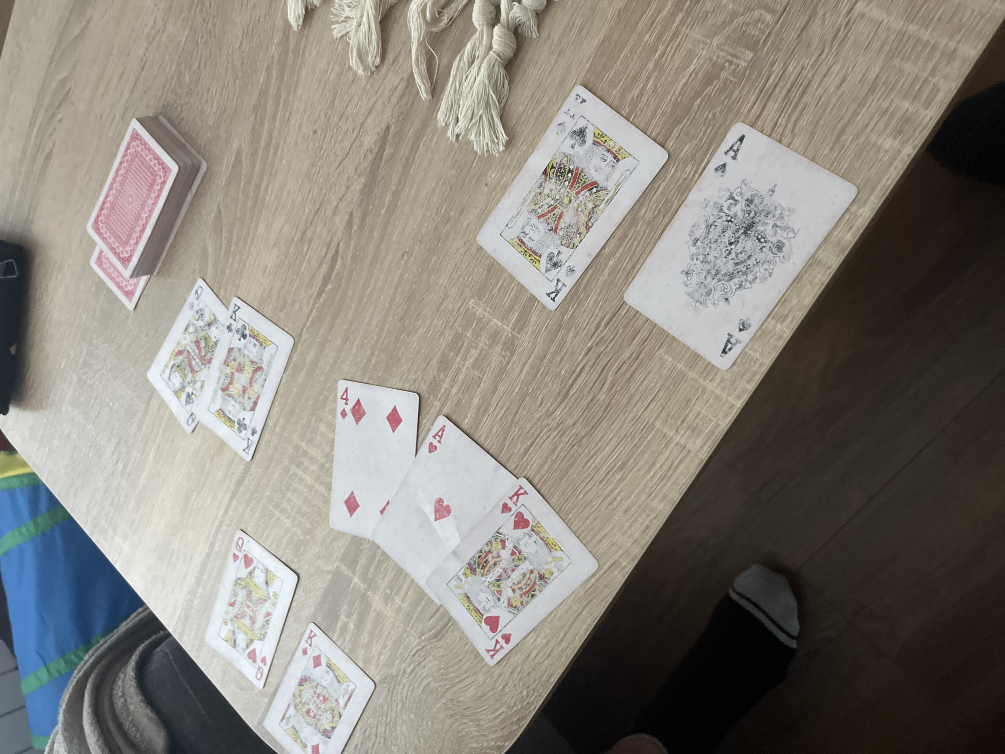 The image shows a light brown wooden table with a deck of red-backed playing cards. There is a pile of the deck in the upper left. Scattered across the table are multiple playing cards: King of Spades, Ace of Spades, King of Hearts, Ace of Hearts, 4 of Diamonds, Queen of Hearts and King of Diamonds.
The context of the location in Plovdiv, Bulgaria is unknown. There is also no evidence of any persons in the image.