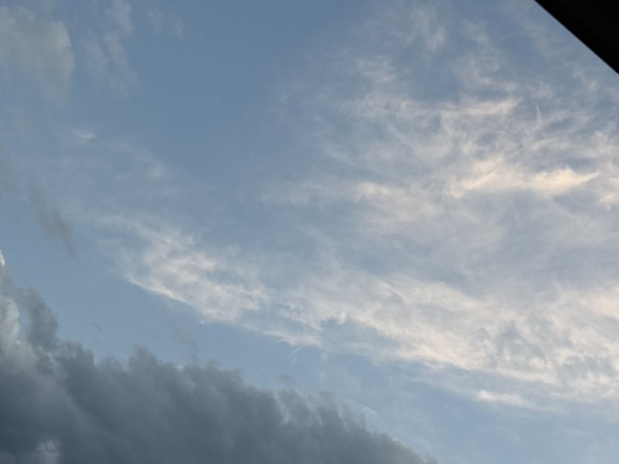 The image displays a cloudy sky over Plovdiv, Bulgaria. In the lower portion of the image, dark, heavy clouds are present, suggesting potential rain or a storm. Above these darker clouds, lighter, wispy clouds are scattered across a pale blue sky. The lighting suggests it is either early morning or late afternoon. There are no people, subjects, or specific objects visible in the scene, only the natural environment of the sky. The angle of the shot suggests it was taken looking upwards.