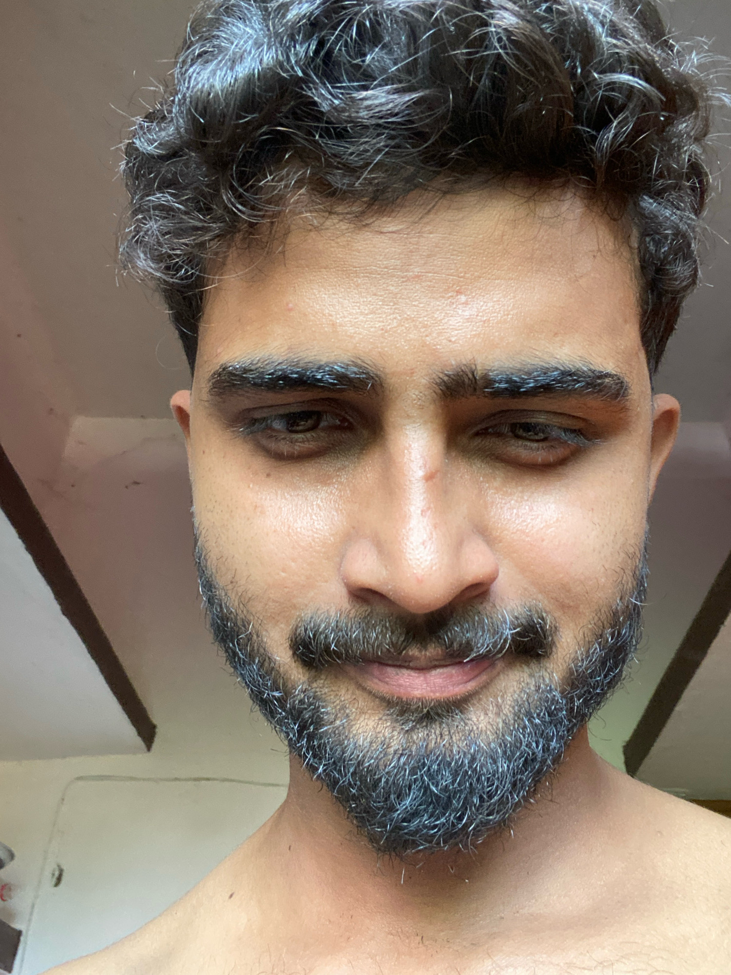 The image is a close-up, headshot of a man with dark, curly hair and a salt-and-pepper beard. He has a light complexion and dark eyes. The background appears to be an indoor setting with a ceiling that has visible wooden beams. The image is taken from a slightly downward angle. There is no specific indication of Bahadurpur, India, in the image itself.