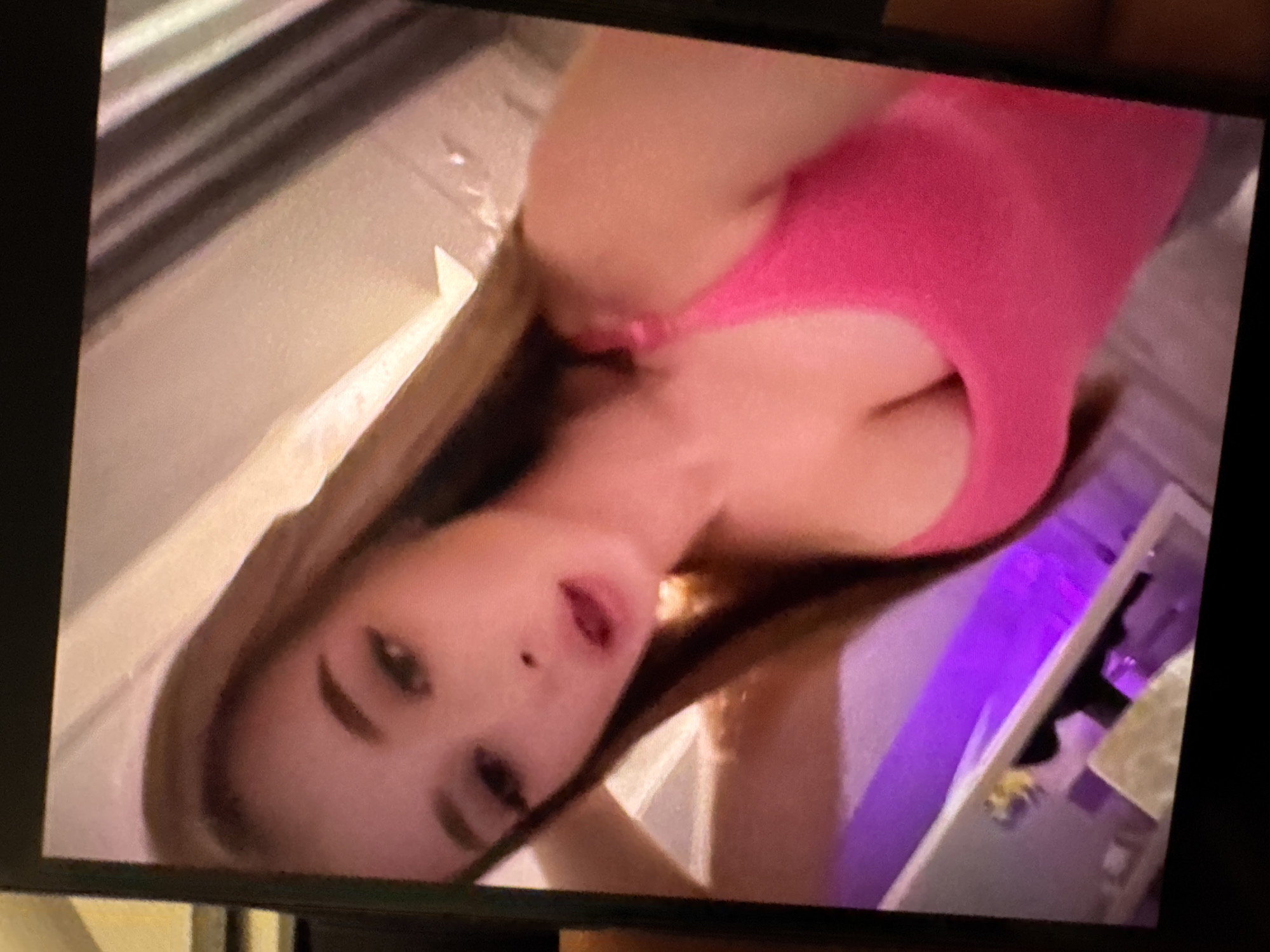 A woman with long, light brown hair and fair skin is wearing a pink tank top. The background appears to be a room with a purple light fixture. The image is rotated. There is no information to identify the location as Yerevan, Armenia, or any information about actions or interactions.