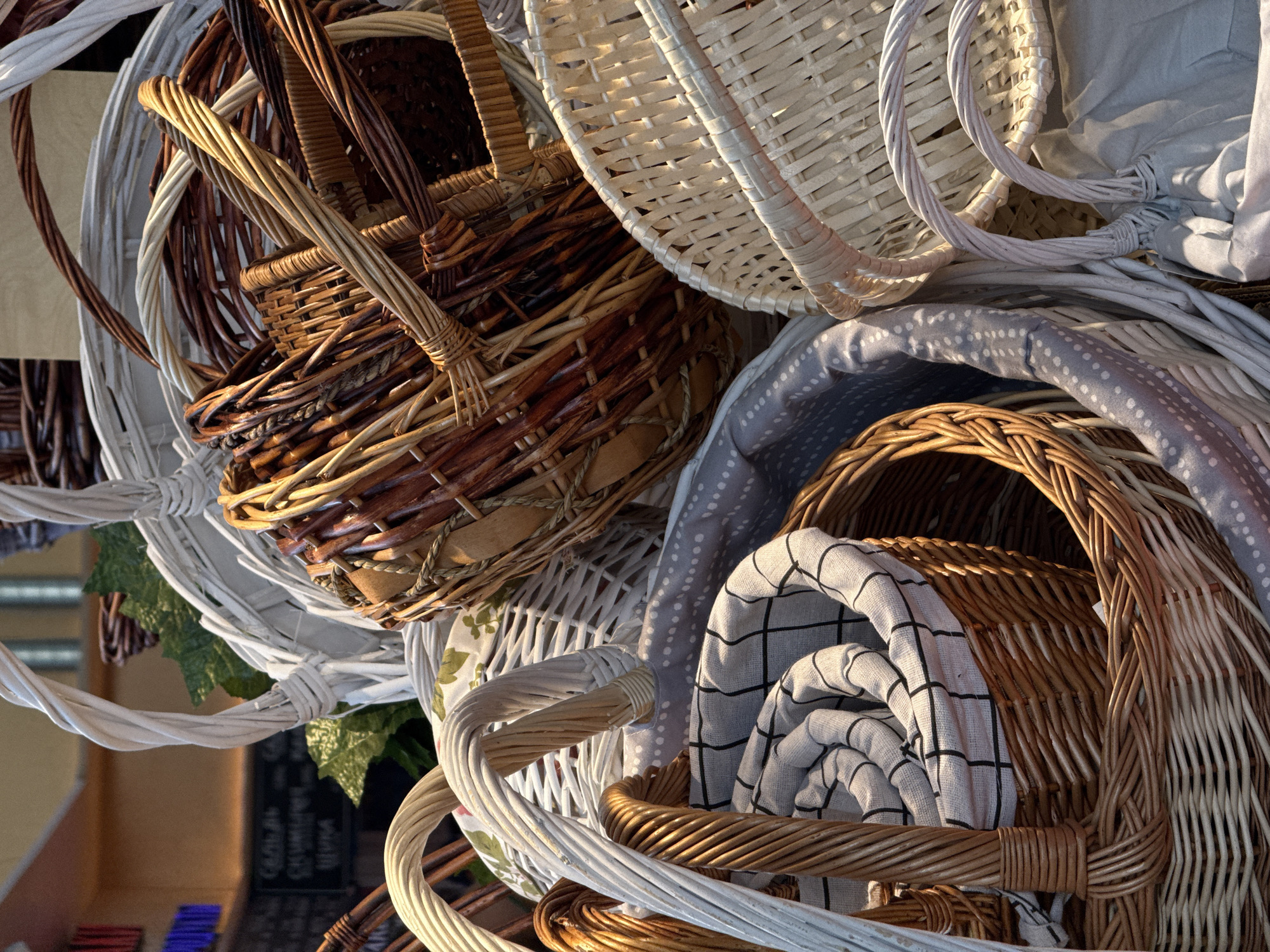 The image shows a pile of various woven baskets, some with fabrics inside. The baskets are in different colors and patterns, ranging from natural brown and tan to white. Some of the baskets have handles. A gray fabric with white polka dots and a white fabric with black gridlines are visible within some of the baskets. The image also captures glimpses of a sign with text on it. The setting appears to be in Moscow, Russia, due to the specific sign with text.