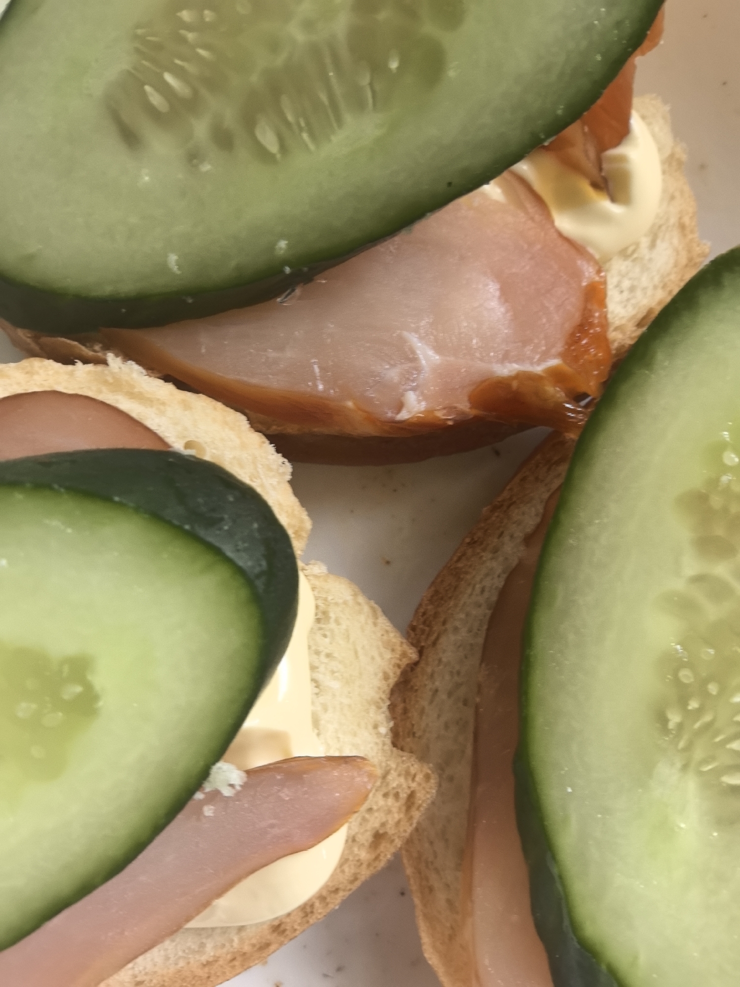 The image shows three open-faced sandwiches on what appears to be toast. Each sandwich is topped with a slice of ham and mayonnaise, and covered with a slice of cucumber. The sandwiches are arranged close together. No people are visible. The location in Noviy, Russia, cannot be determined from the image.