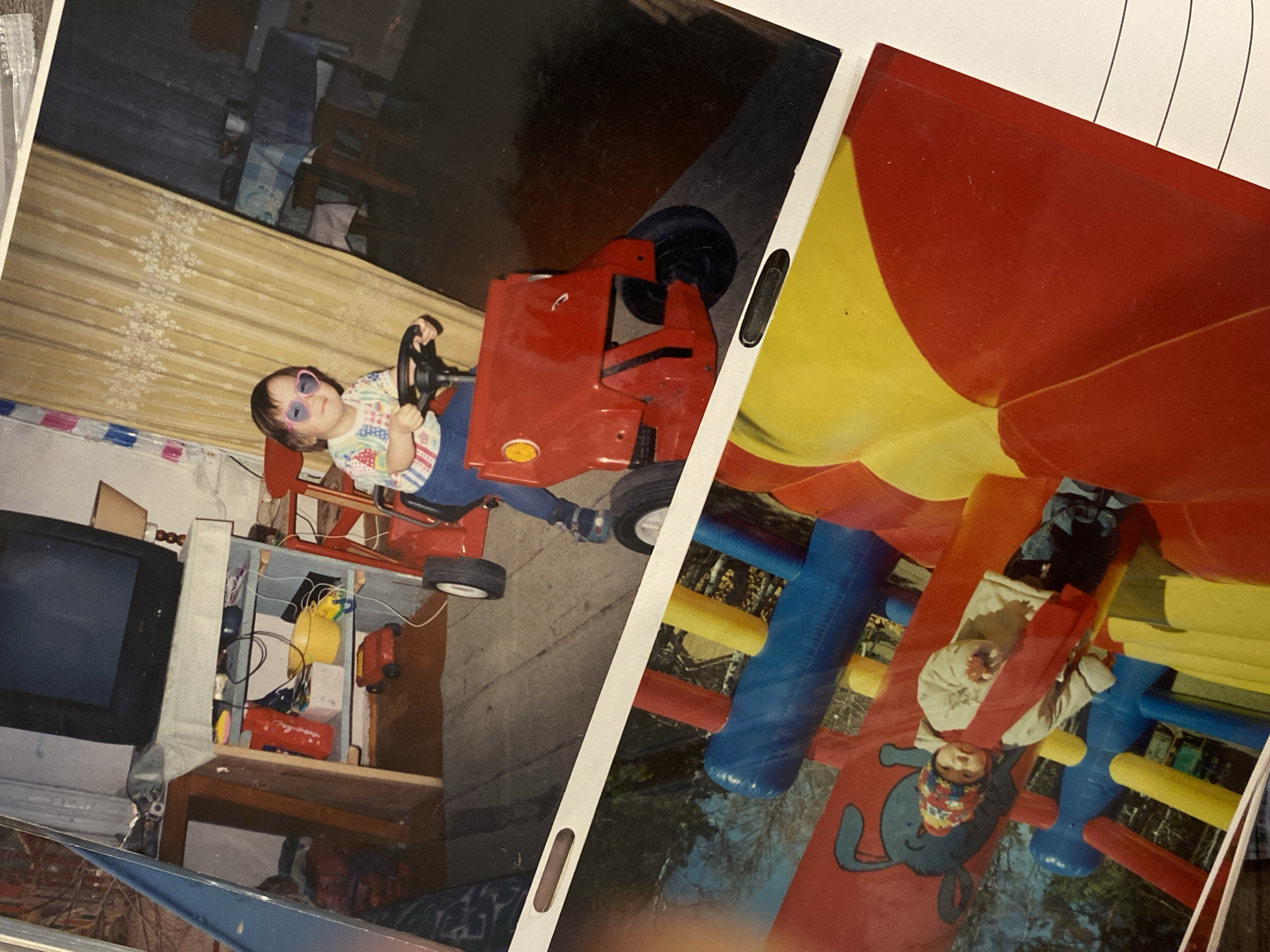 The image shows two photographs slightly overlapping each other.
Photograph 1 depicts a young child wearing heart-shaped sunglasses and a patterned top sitting in a red toy tractor indoors. A television and a shelf containing toys are visible in the background.
Photograph 2 features a child in winter clothing on a colorful inflatable playground, possibly an indoor play area. The playground has red, yellow, and blue elements.
The location and city cannot be determined from the image. The image's content is unrelated to the city of Krasnoyarsk, Russia.