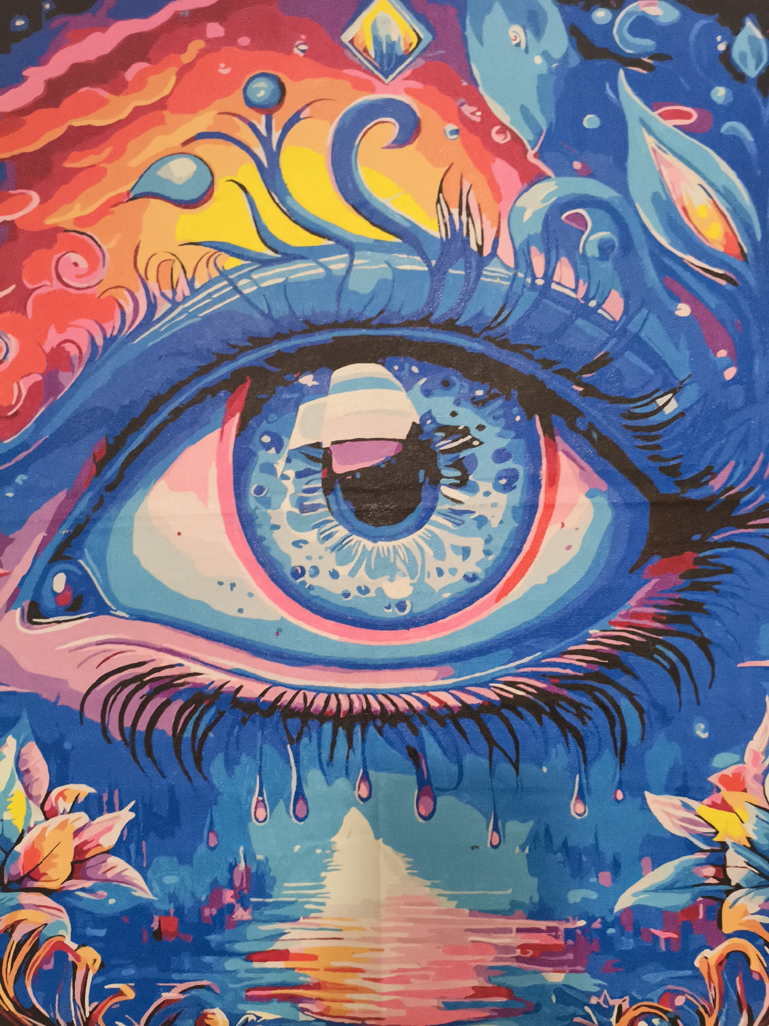 The image presents a close-up of a stylized, oversized eye painted in various shades of blue, pink, yellow, and black. The eye dominates the composition, with detailed eyelashes and a multilayered iris reflecting a scene of white stripes. Above the eye are swirling patterns and shapes suggesting clouds, water, or abstract organic forms. Below the eye, stylized teardrops fall onto a landscape with reflections, possibly representing a city or waterfront scene. The colors in this lower section include shades of blue, pink, yellow and white. At the bottom corners, there are stylized floral elements. It is unknown where the image was taken in the city of Nowy Tomyśl, Poland.