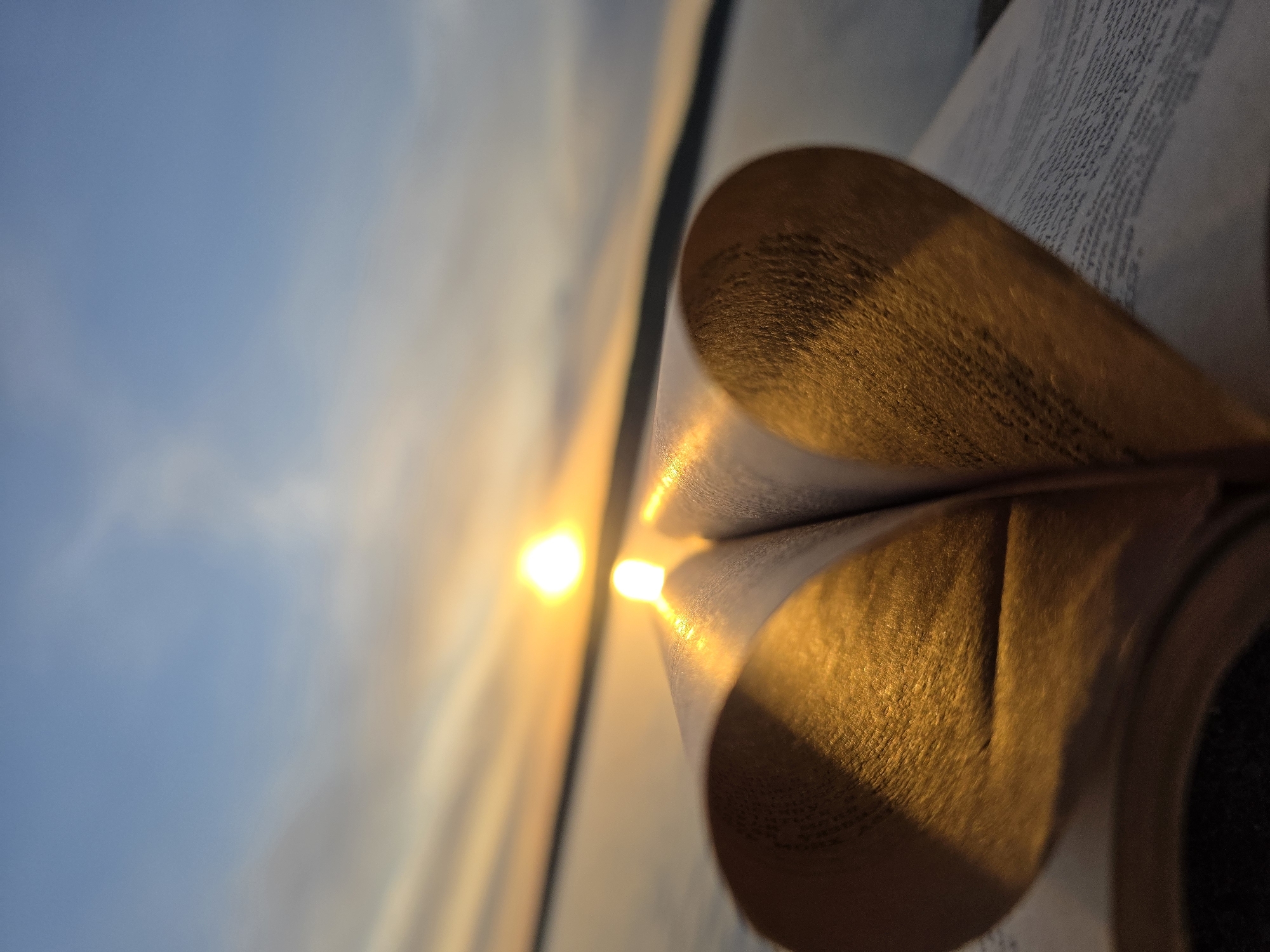 The image shows an open book with pages folded into a heart shape. Sunlight illuminates the heart from the left. The book is positioned against a backdrop of a blurred sky. Based on the location specification of Chaikovsky, Russia, the image may be taken there, although nothing in the photo confirms that specific location.