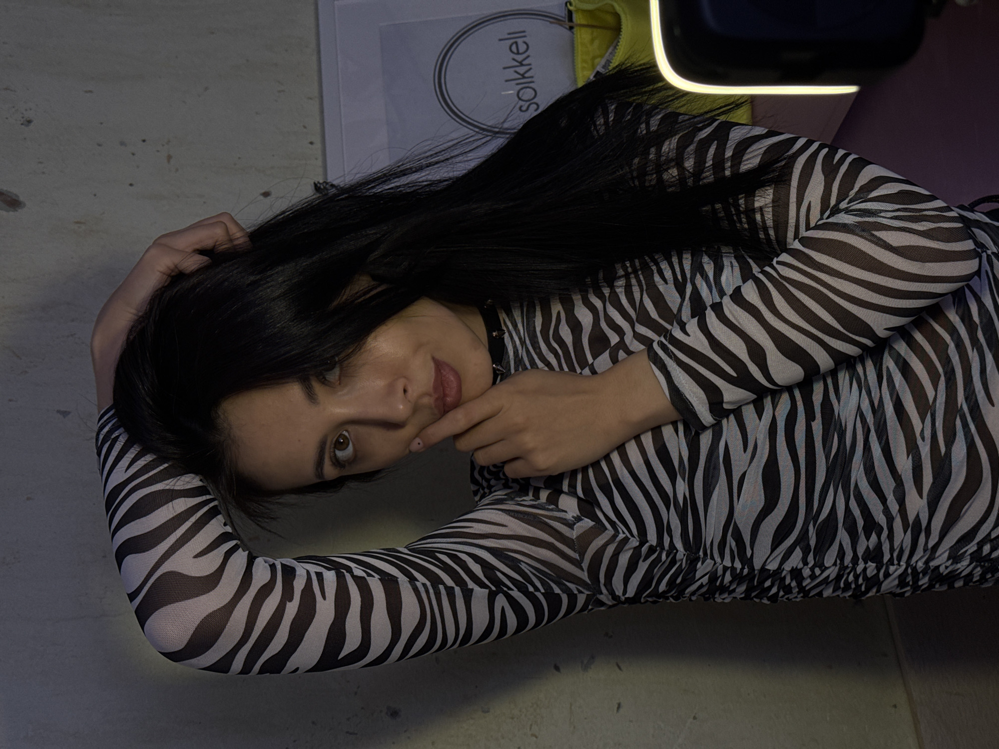 A woman with dark hair and a zebra-print top is lying on a surface with a shopping bag from "Sokkelii" partially visible. The bag and the presence of "Sokkelii" suggest the image was likely taken in a city with a Sokkelii store. While the photograph itself cannot definitively confirm the exact location, the store name could offer information about the location. The city of Votkinsk, Russia, is not confirmed from the information in the image, but can be implied because the Sokkelii store exists there.