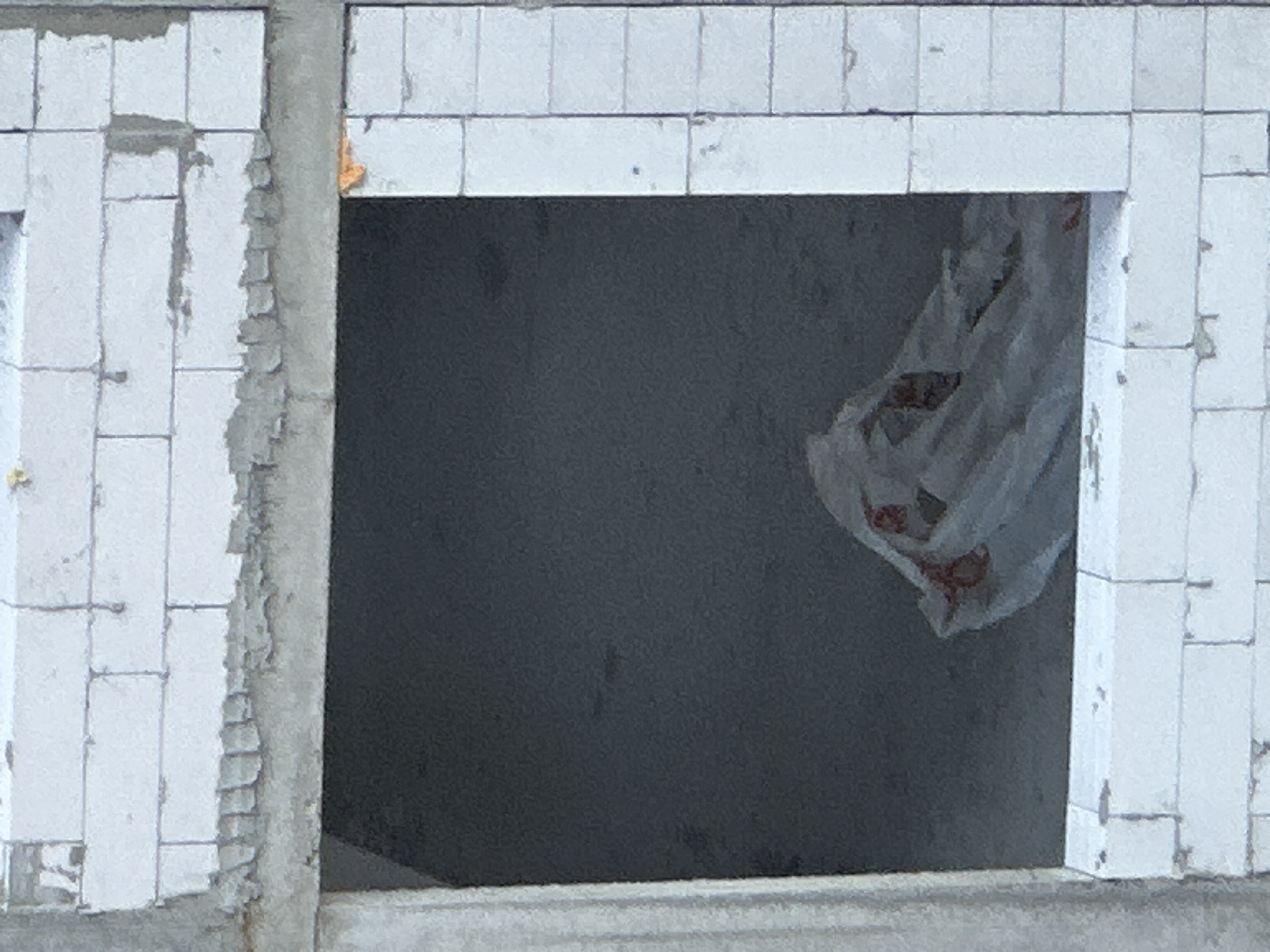 The image shows a partially constructed building with an open window. The building is made of white cinder blocks. Inside the window, a crumpled white plastic bag with red markings is visible. The scene is likely in Kyiv, Ukraine, given the context. The construction appears to be ongoing, as evidenced by the exposed materials and the unfinished state of the building.