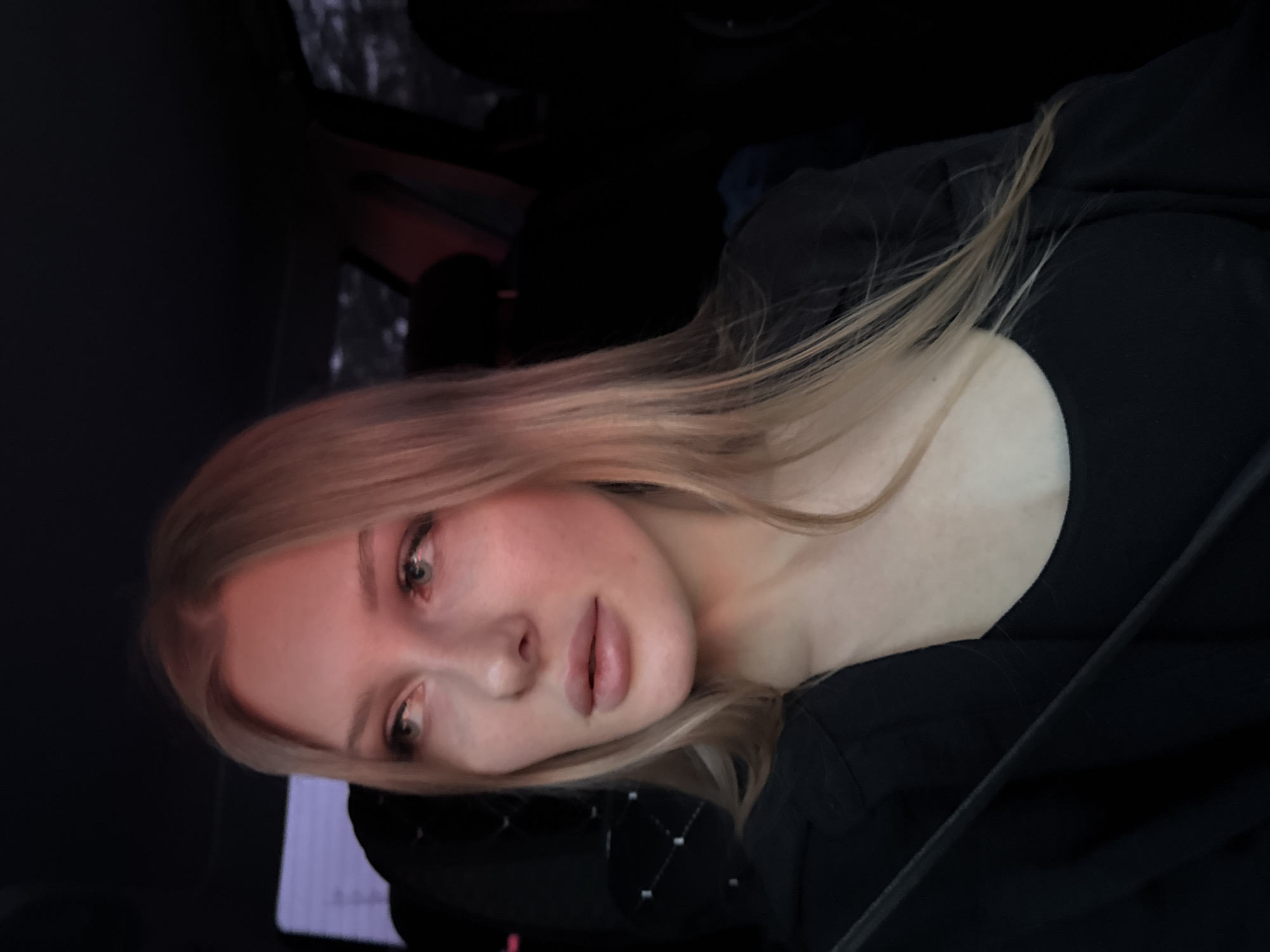 A fair-skinned young woman with blonde hair is seated in a car, wearing a black low-cut top and a seatbelt. She is looking towards the camera with a neutral expression. The interior of the car is dark and somewhat indistinct. The location, Perm, Russia, cannot be determined from the visible details in the image.