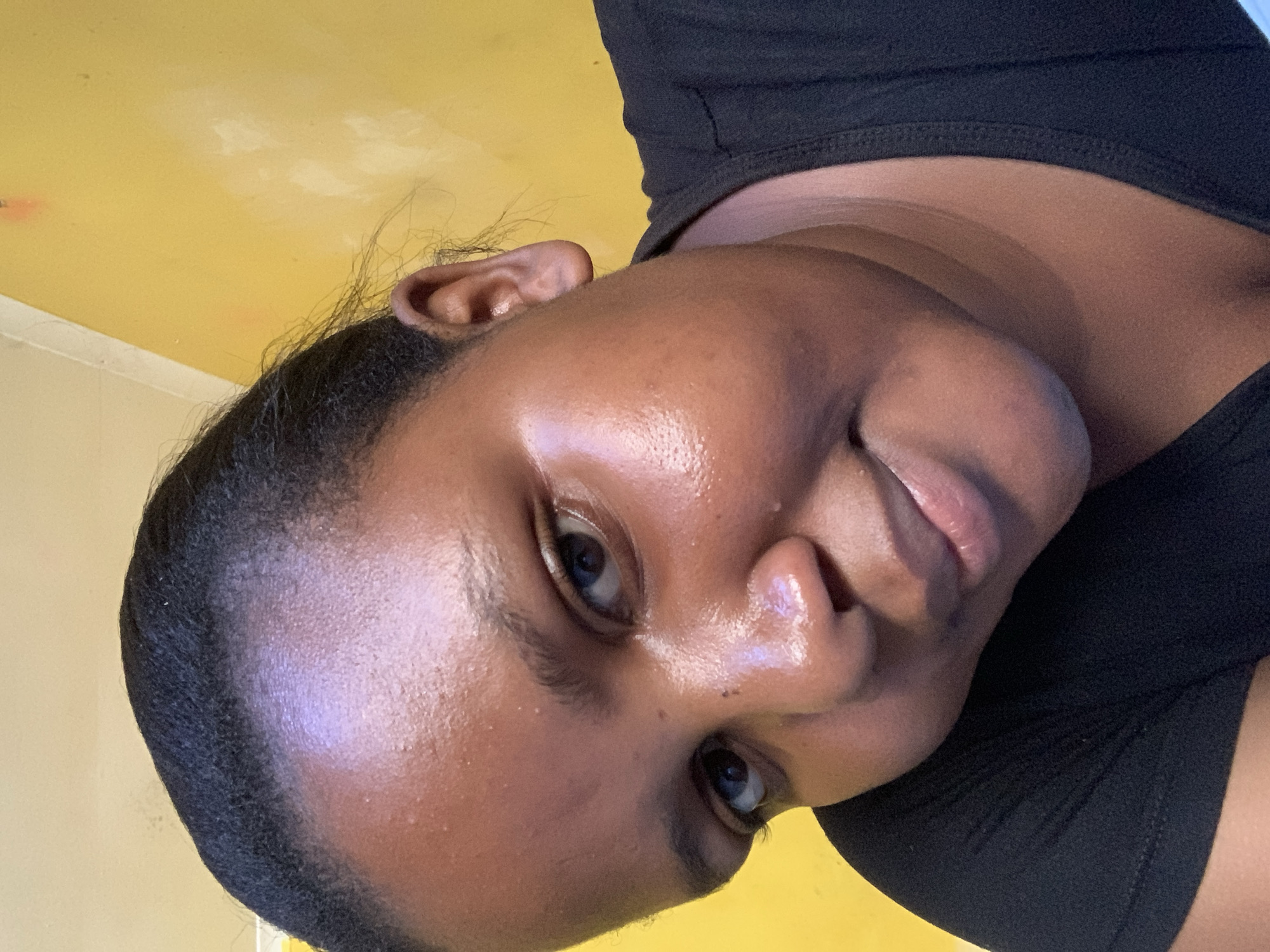 A person with dark skin is angled in front of a yellow wall. The person is wearing a black shirt. The image lacks sufficient information to determine a location in Dar es-Salaam, Tanzania.