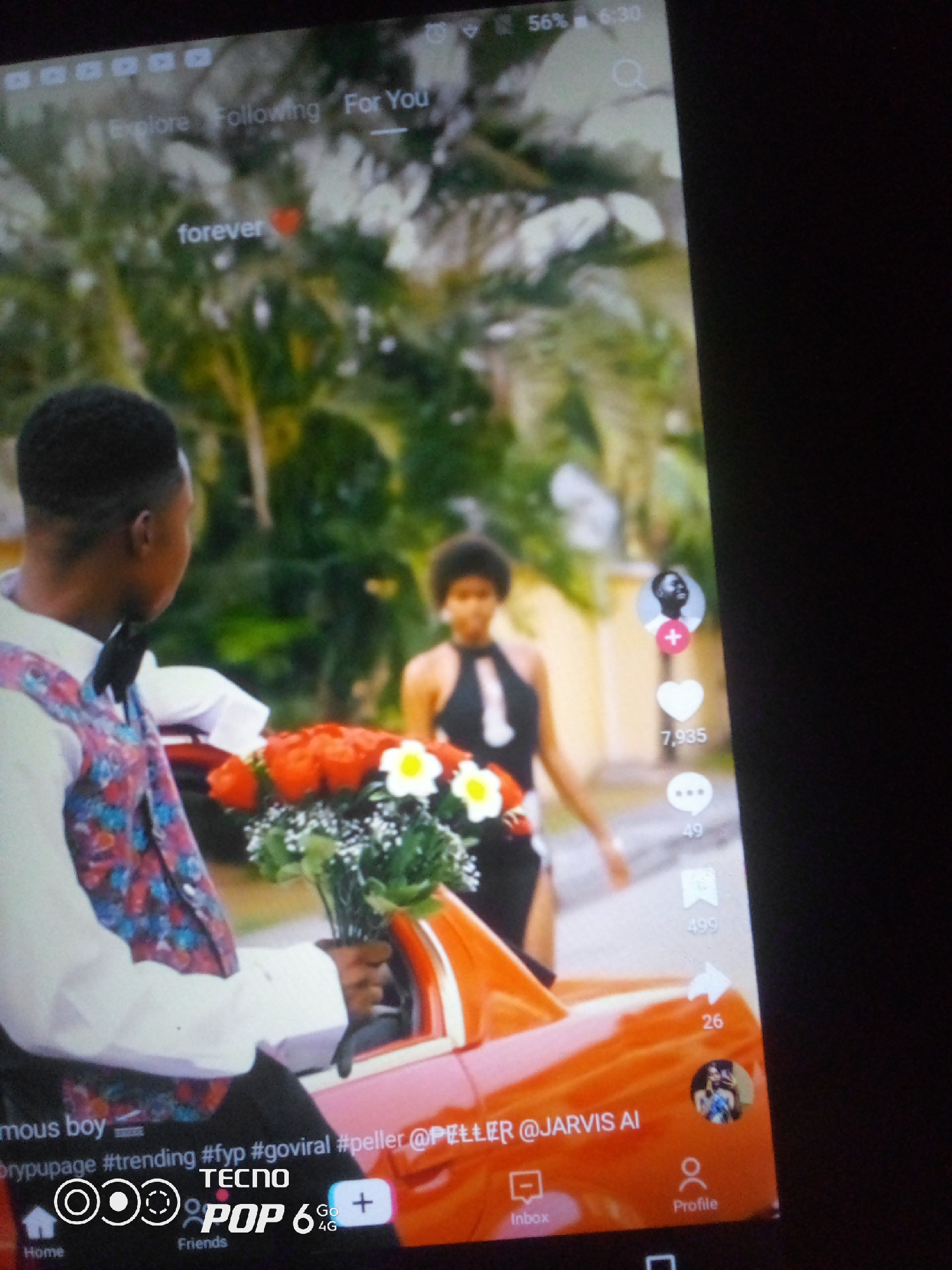 A man wearing a white shirt, a colorful vest, and a black bowtie holds a bouquet of red roses in front of an orange convertible. A woman in a black and white dress stands in the background. The scene appears to be outdoors, with lush green foliage. The image is a screenshot from a social media platform, likely TikTok, indicated by the interface elements such as the "For You" tab, icons for likes, comments, and shares, and the user profile picture. The bottom of the screen displays navigation icons for "Home," "Friends," and "Inbox," along with a Tecno Pop 6 4G logo. The timestamp at the top shows "56% 6:30". The image does not provide any information about the location being Howayi, Nigeria.