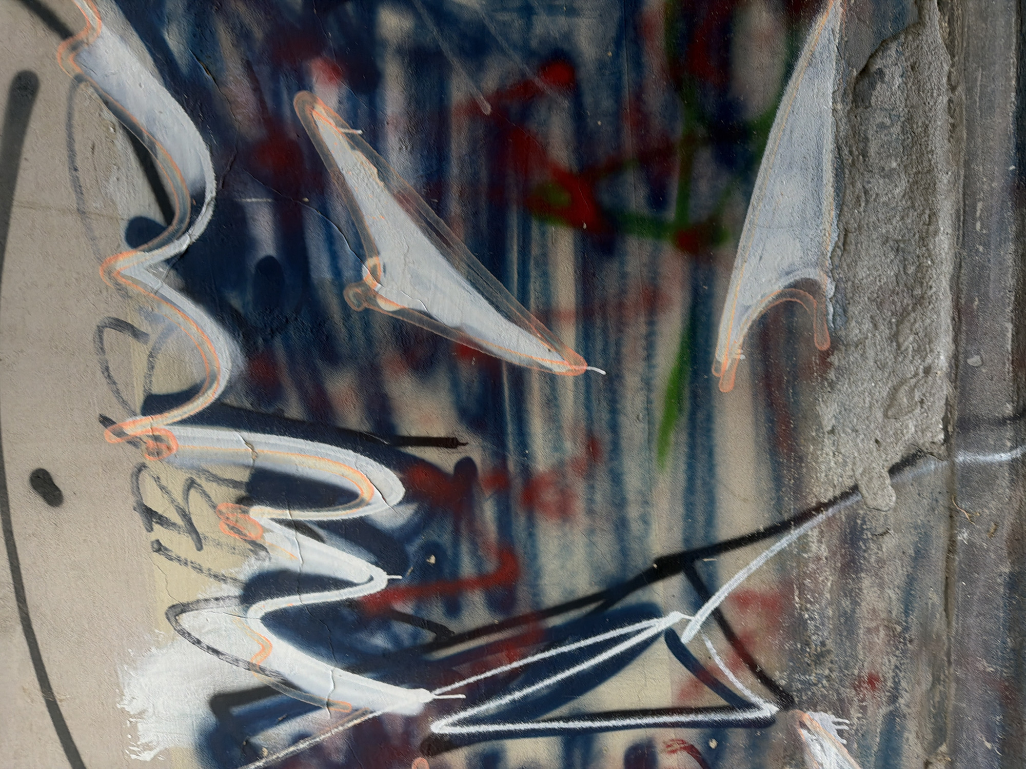 Close-up of graffiti on a concrete wall in Belgrade, Serbia. The graffiti consists of white and black painted lines, some forming triangular shapes, overlaid on a background of blue, red, and green paint streaks. The concrete wall shows signs of weathering and cracking.