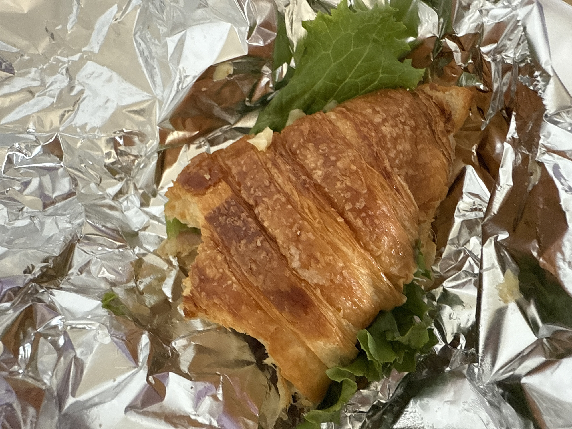 A croissant sandwich rests on aluminum foil. The sandwich contains lettuce. The location is Puebla, Mexico.