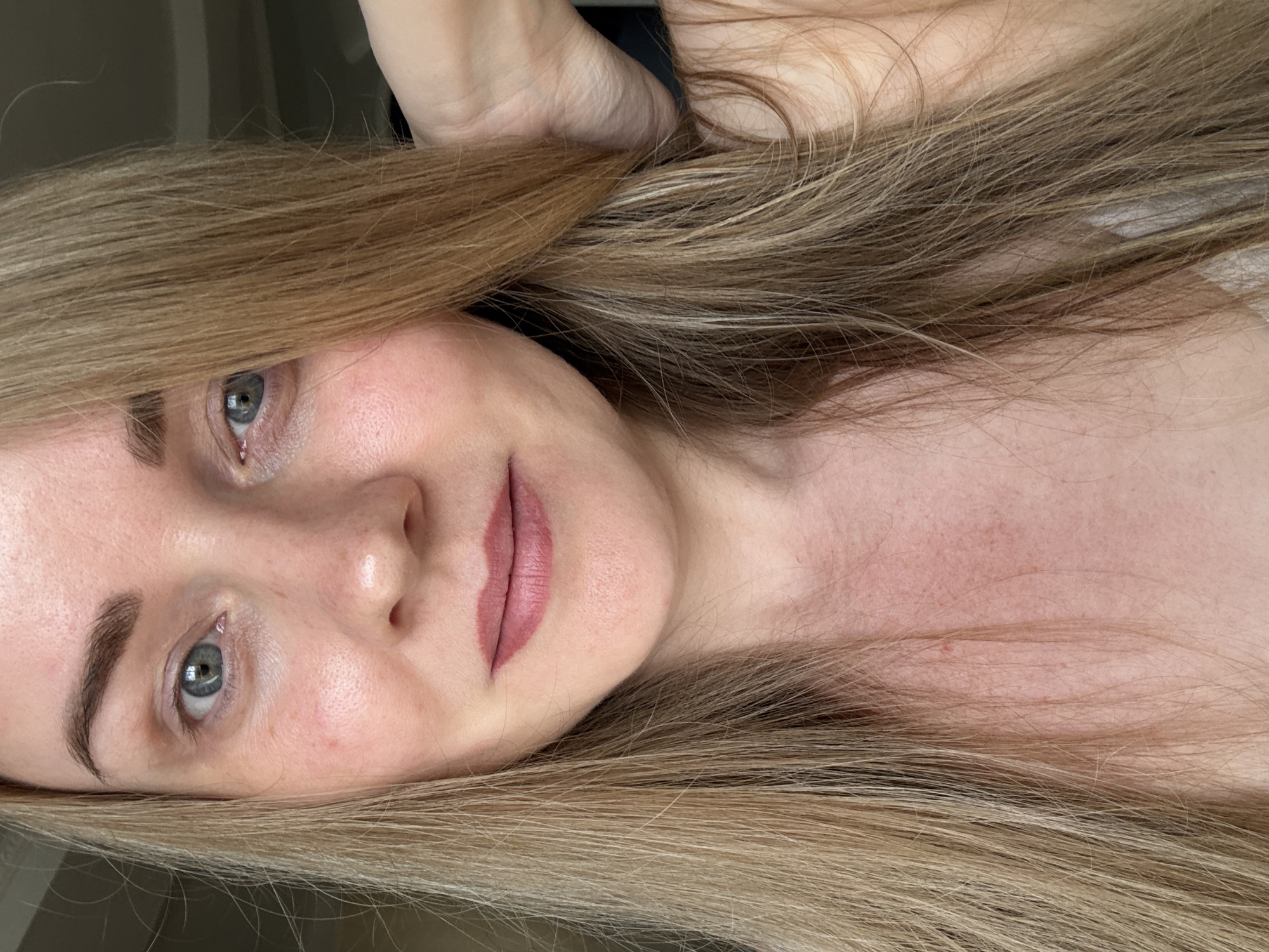 A close-up, slightly rotated selfie of a woman with long blonde hair. Her facial features include light grey eyes, noticeable eyebrow hairs, and lips coated in light pink lipstick. The background is out of focus and indistinct. There is no evidence to suggest this image was taken in the city of Chaikovsky, Russia.