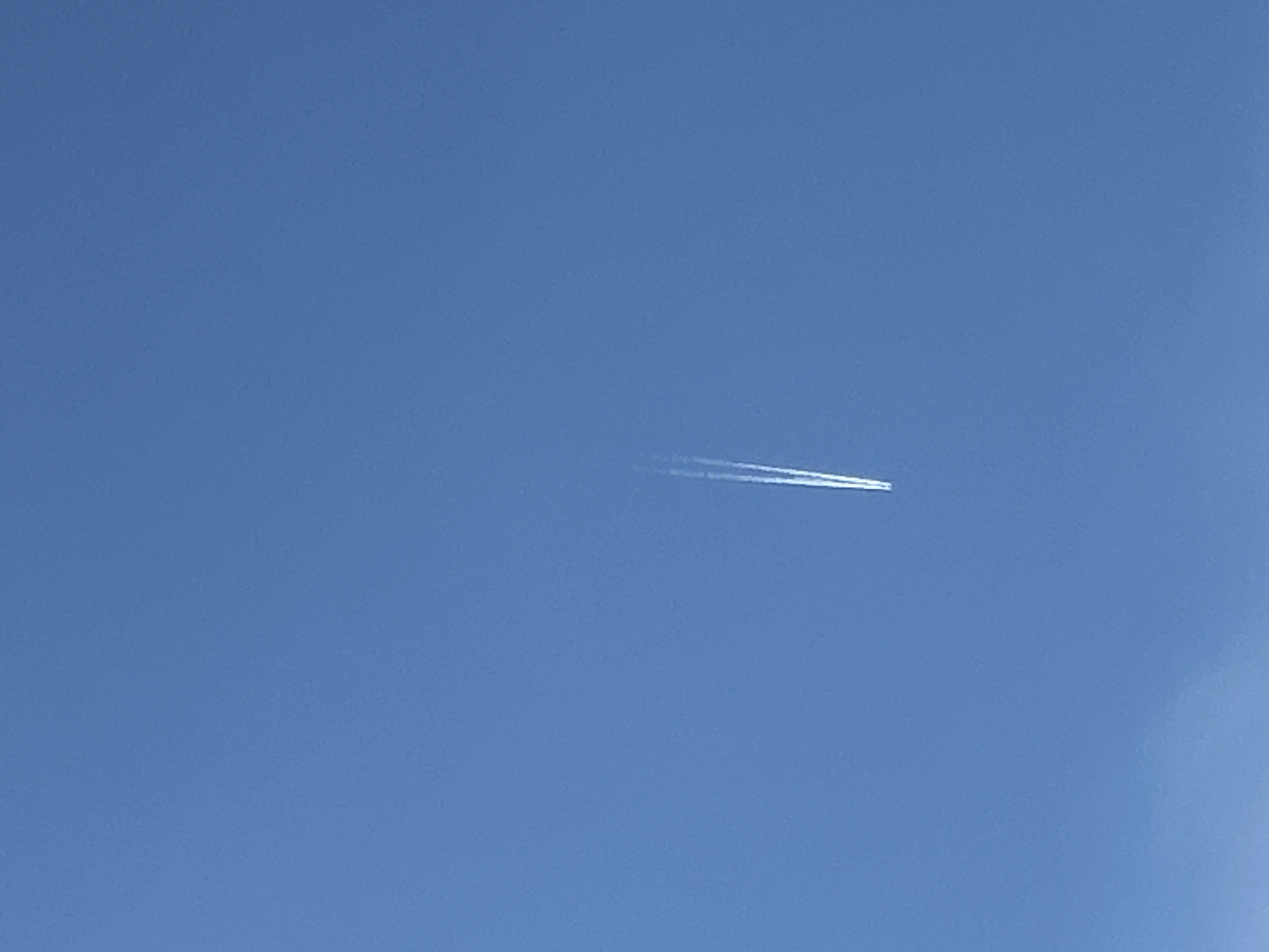 The image shows a bright blue sky with a contrail, presumably from a jet airplane, moving horizontally across the center of the frame. The contrail is white and appears slightly diffused. The sky is clear with minimal cloud cover. The location is assumed to be Plovdiv, Bulgaria. No people or other objects are visible.