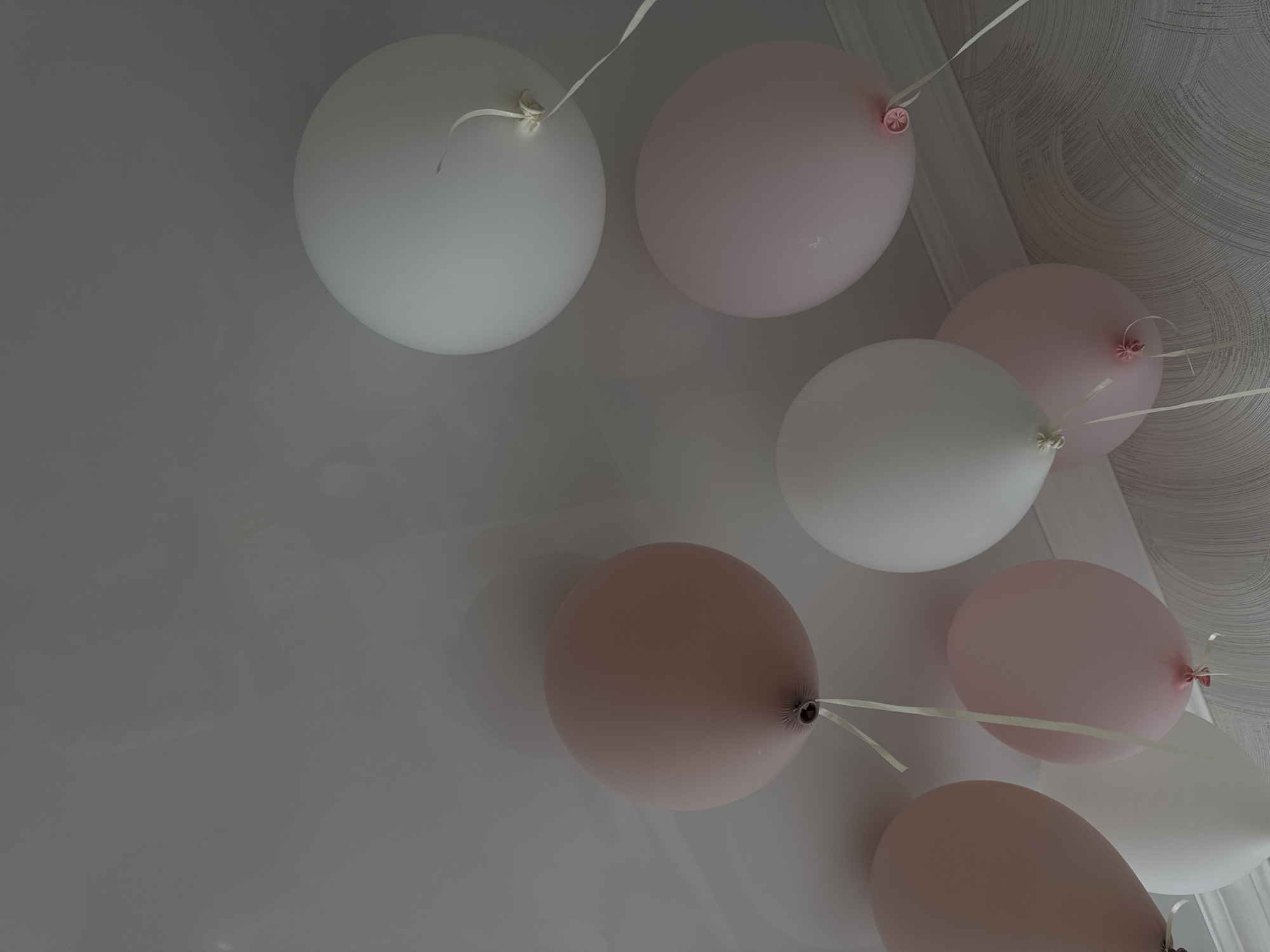The image shows a group of balloons, with white and pink colors, attached to a ceiling with white ribbons. The ceiling appears to be textured. The location in the city of Sochi, Russia cannot be determined from the image. There are no people or other subjects depicted.