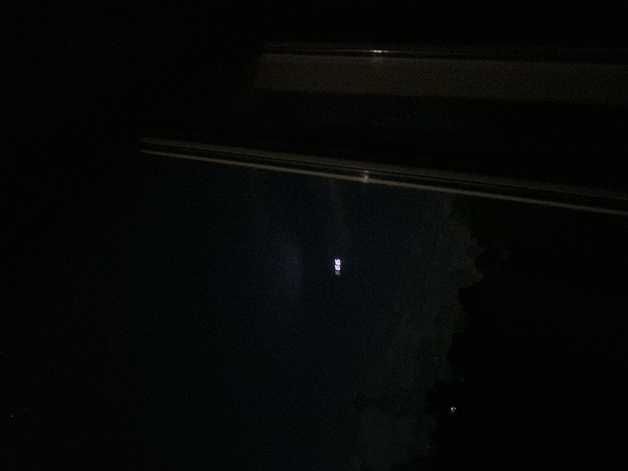 The image depicts a dark, possibly nighttime scene. In the upper part of the frame, a rectangular shape, possibly a window or part of a building, is visible. Near the center of the frame, a pair of bright lights, arranged vertically, are present. Some dark objects with uneven edges are visible in the bottom right corner. There is no indication of people, actions, or interactions in the frame. There are no details from which to determine the location in the city of Loznitsa, Bulgaria.