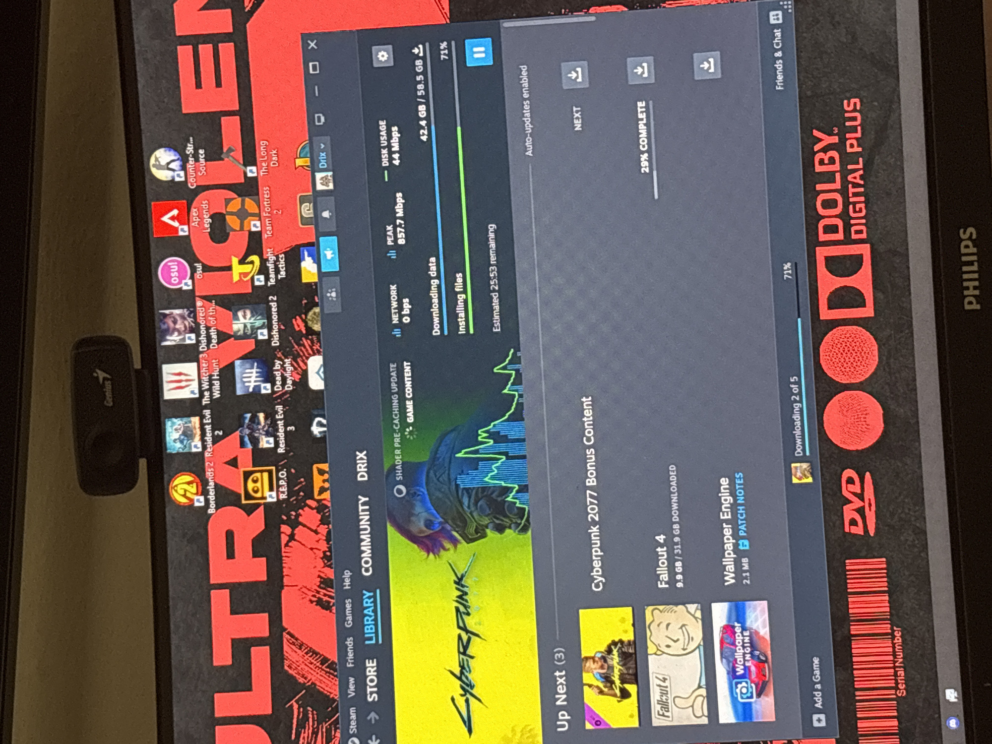 The image shows a computer screen displaying the Steam game client. The screen features a red and black wallpaper with the word "ULTRA" prominently displayed. Various game icons are visible at the top, including Borderlands 2, Resident Evil 2, The Witcher 3, and Apex Legends. The Steam client shows a download progress bar for "Cyberpunk 2077 Bonus Content," which is 71% complete and has an estimated 25 minutes and 53 seconds remaining. Below this, "Fallout 4" is listed with 9.9 GB downloaded out of 31.9 GB. "Wallpaper Engine" is also visible. The bottom of the screen shows the "Dolby Digital Plus" logo and the "Philips" brand. There is no indication of the location being Karviná, Czechia. The image is a close-up, frontal view of the computer monitor.