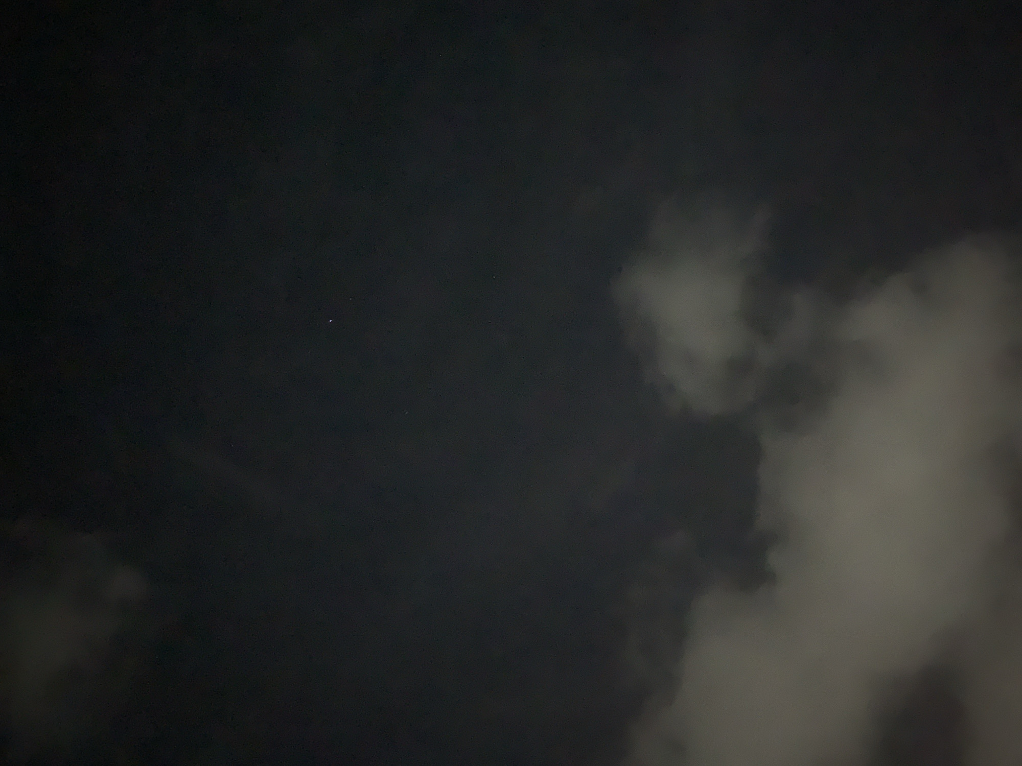 The image shows a dark night sky. In the center-left area of the frame are two visible stars. To the right, there are cloud formations. The bottom left also has some cloud cover. I have no information that would allow me to determine location in the city of Santa Ana, Venezuela.