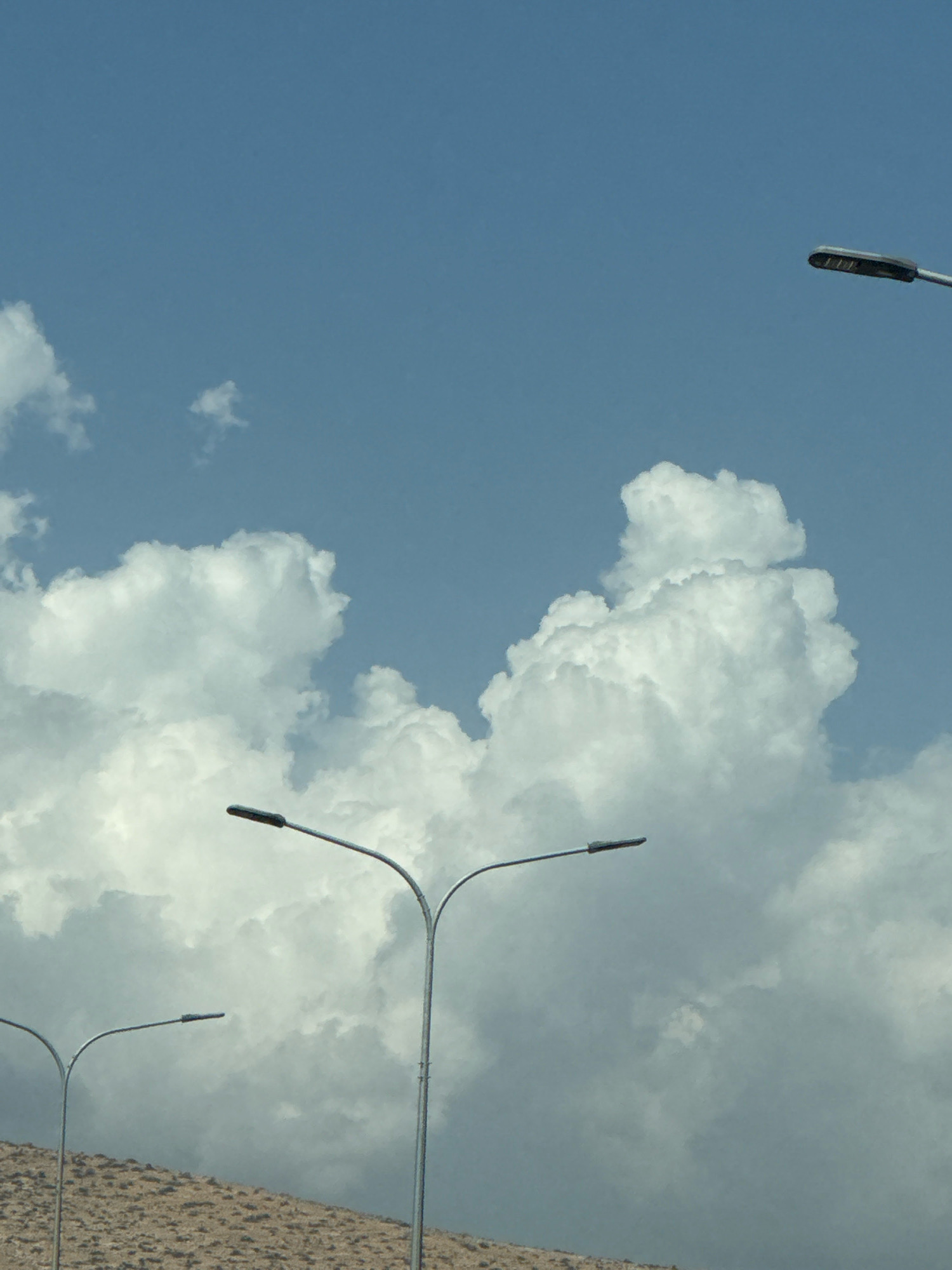 The image shows a sky with scattered clouds and several streetlights. The landscape beneath the sky appears to be a dry, rocky hillside. There are no people or animals visible in the image. The scene is devoid of any specific indicators that would place it in Germasogeia Municipality, Cyprus.