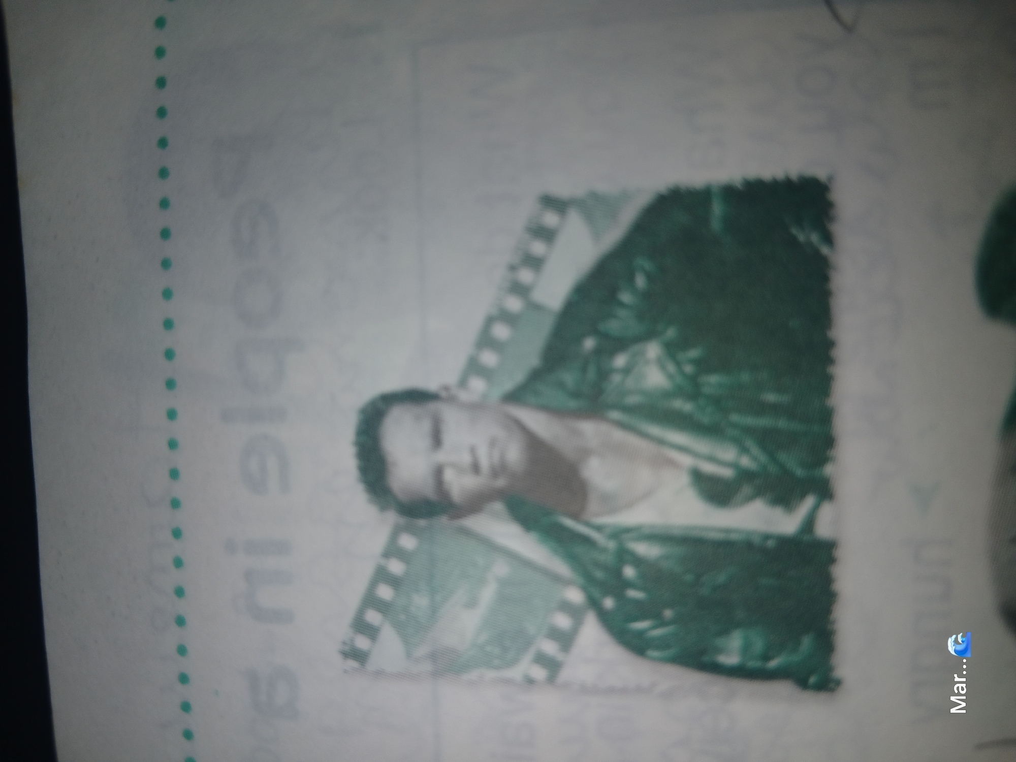 The image is a close-up of a printed page, likely from a book or magazine, with a photograph of actor Arnold Schwarzenegger at its center. He is depicted wearing a leather jacket over a tank top, with a film strip visible behind him. The background of the page contains faint text and some dotted lines. In the lower left corner of the page, the text "Mar..." is visible, followed by a wave emoji. There is no visible information or imagery that would indicate a location in La Tagua, Venezuela.