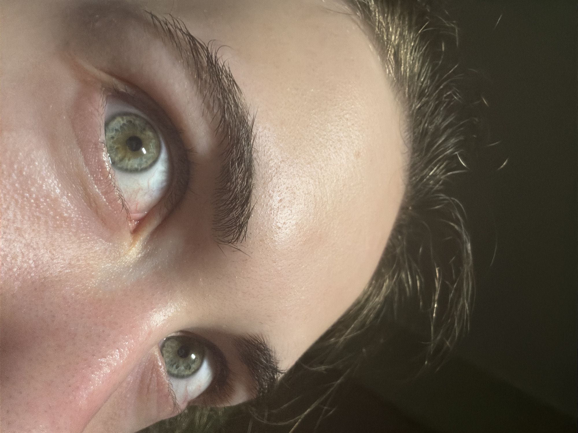 This is a close-up, overhead shot of a person's eyes and forehead. The person has light-colored skin and dark hair. The eyes are wide open and appear to be green. The background is dark and out of focus. There is no visible indication of the city of Zavodoukovsk, Russia.