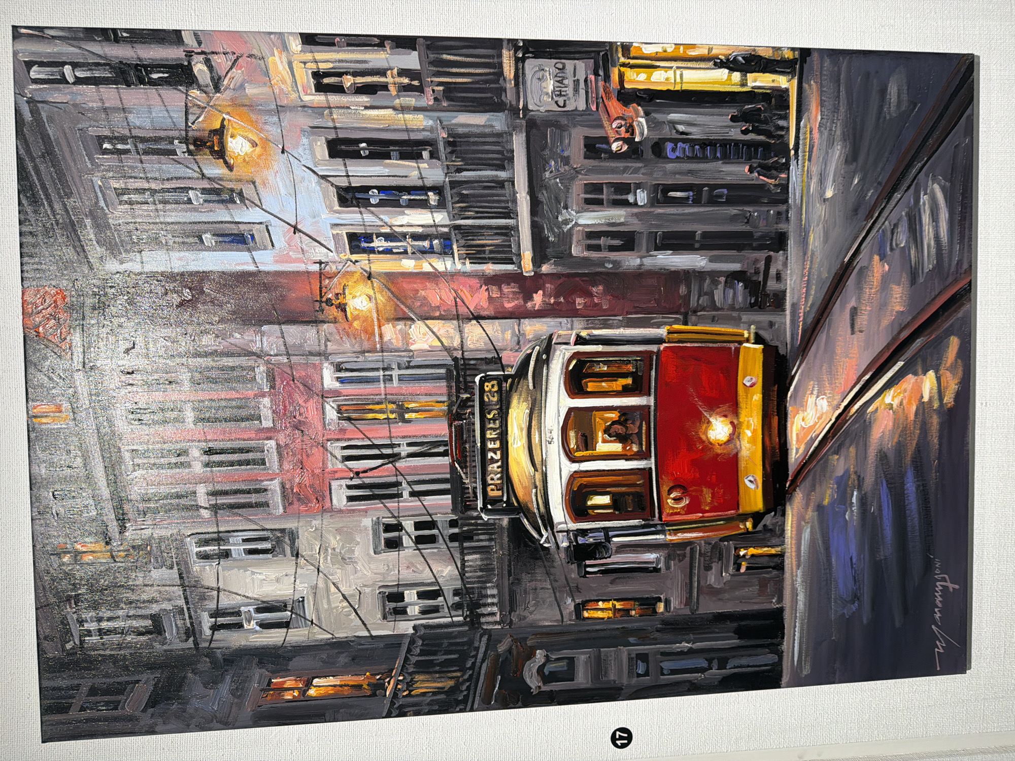 This is an oil painting depicting a street scene at night with a red and yellow tram as the central subject. The tram has "PRAZERES 28" written on its front sign. The tram is on tracks that run through a narrow street lined with multi-story buildings. The buildings have many windows, some of which are lit, suggesting interiors. Streetlights illuminate the scene, casting warm yellow and orange glows on the buildings and the wet street. Reflections of the lights and the tram are visible on the street surface. Several silhouetted figures can be seen standing on the sidewalk in the background, and one figure is visible inside the tram. The painting's style is impressionistic, with visible brushstrokes. The signature "W. Marignoni" is visible in the lower left corner. While the scene evokes a European city ambiance, there is no specific indication within the painting itself that it is set in Cascais, Portugal; the sign on the tram suggests the Prazeres route, which is famously associated with Lisbon, Portugal.