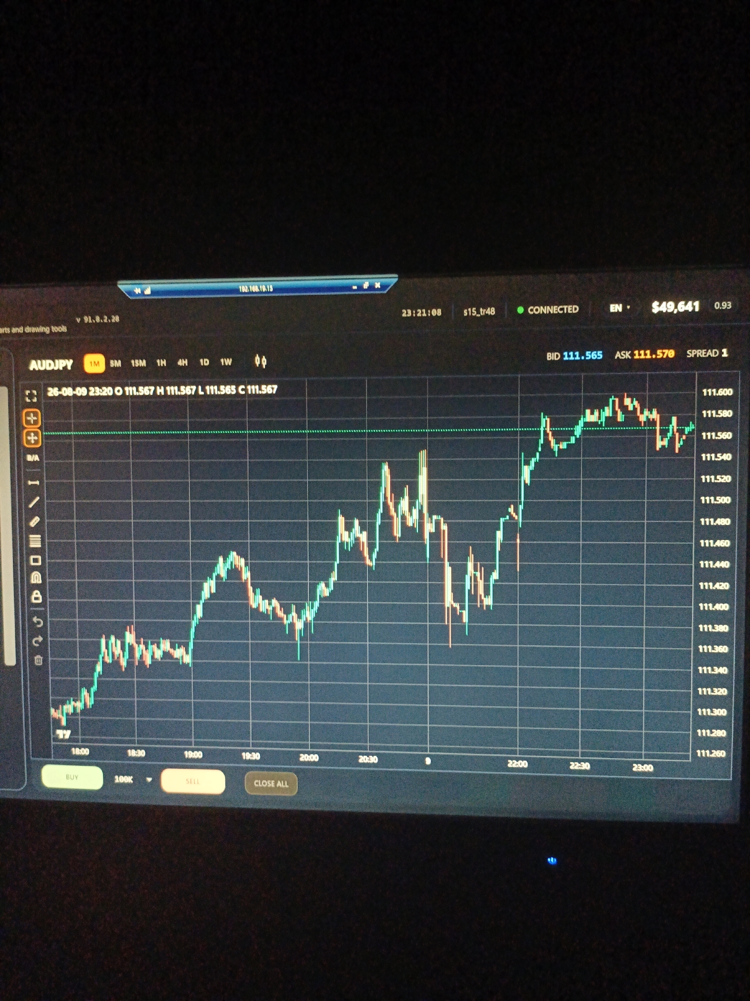 The image shows a close-up of a computer screen displaying a financial trading platform. The screen shows a candlestick chart for the AUDJPY currency pair. The chart displays price movements over a period of time, with green candlesticks indicating price increases and red candlesticks indicating price decreases. The current time is displayed as 23:21:08. The screen also shows the current bid price as 111.565 and the ask price as 111.570. There is a balance of $49,641. The image is taken from a dark room, with only the computer screen illuminated. There is no indication of the location being in the city of Ухманы, Russia.