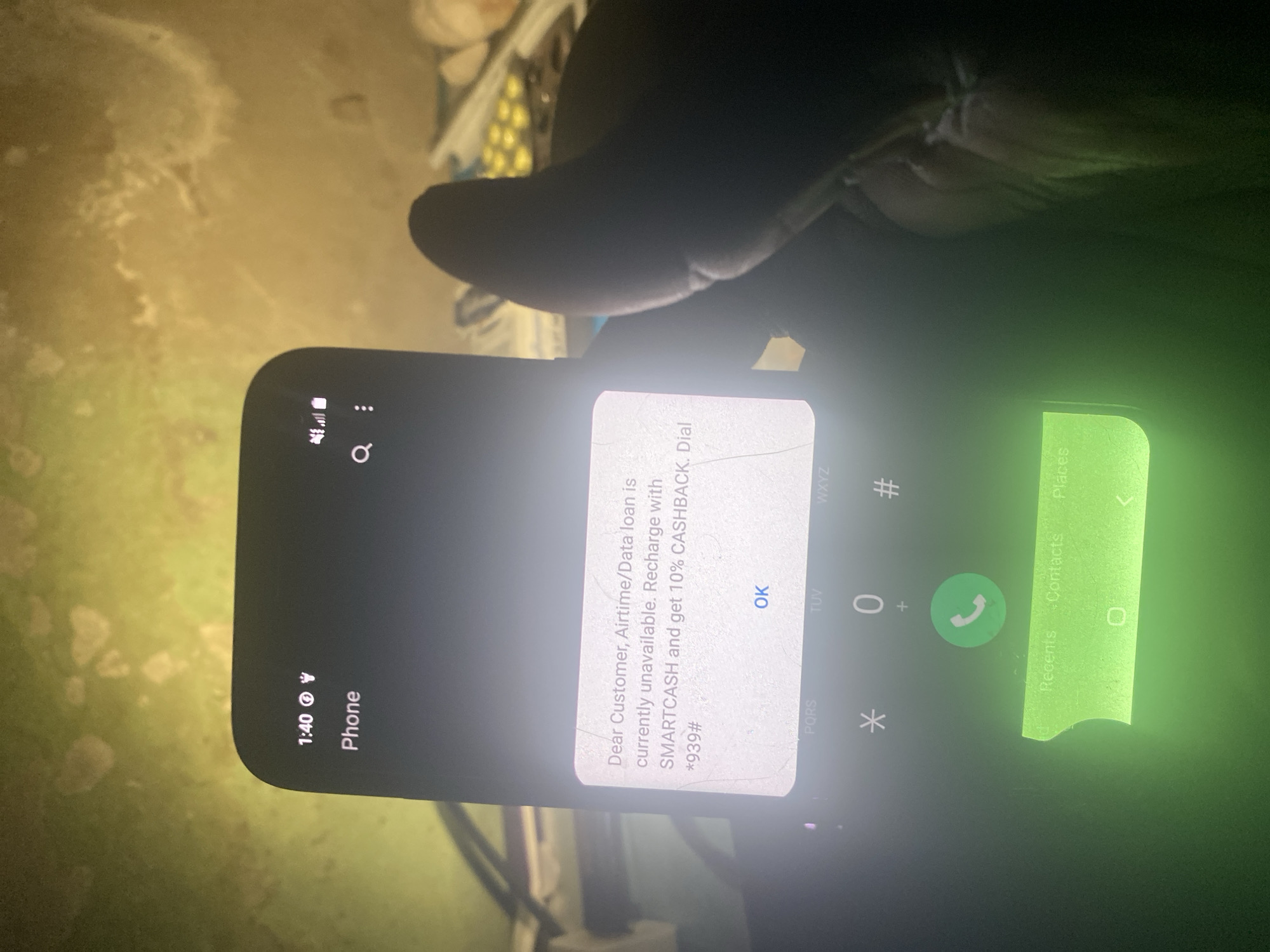 A close-up shot of a smartphone held by a person's hand. The smartphone screen displays a pop-up notification stating "Dear Customer, Airtime/Data loan is currently unavailable. Recharge with SMARTCASH and get 10% CASHBACK. Dial *939#." The notification has an "OK" button. The phone interface below the notification shows the dial pad of a phone application. The time on the phone reads 1:40.