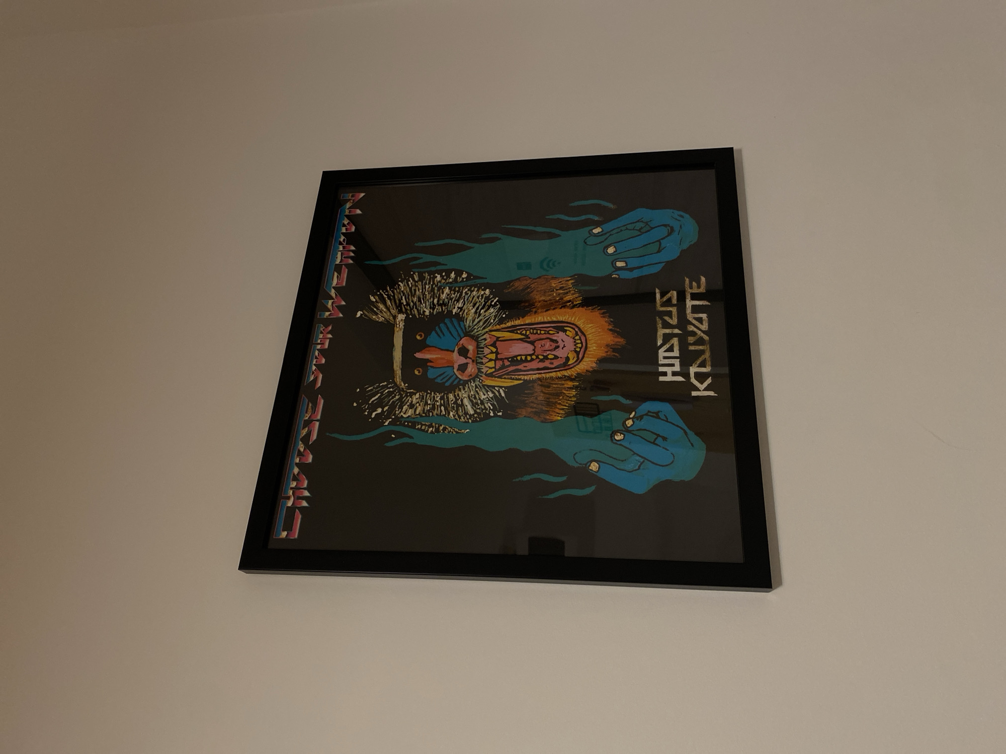 A framed poster hangs on a light-colored wall. The poster features a baboon-like creature with an open mouth, surrounded by turquoise hands. Text reading "Hiatus Kaiyote" is visible on the right. The poster is framed in black. The location in the city of Izhevsk, Russia, cannot be determined from the image.