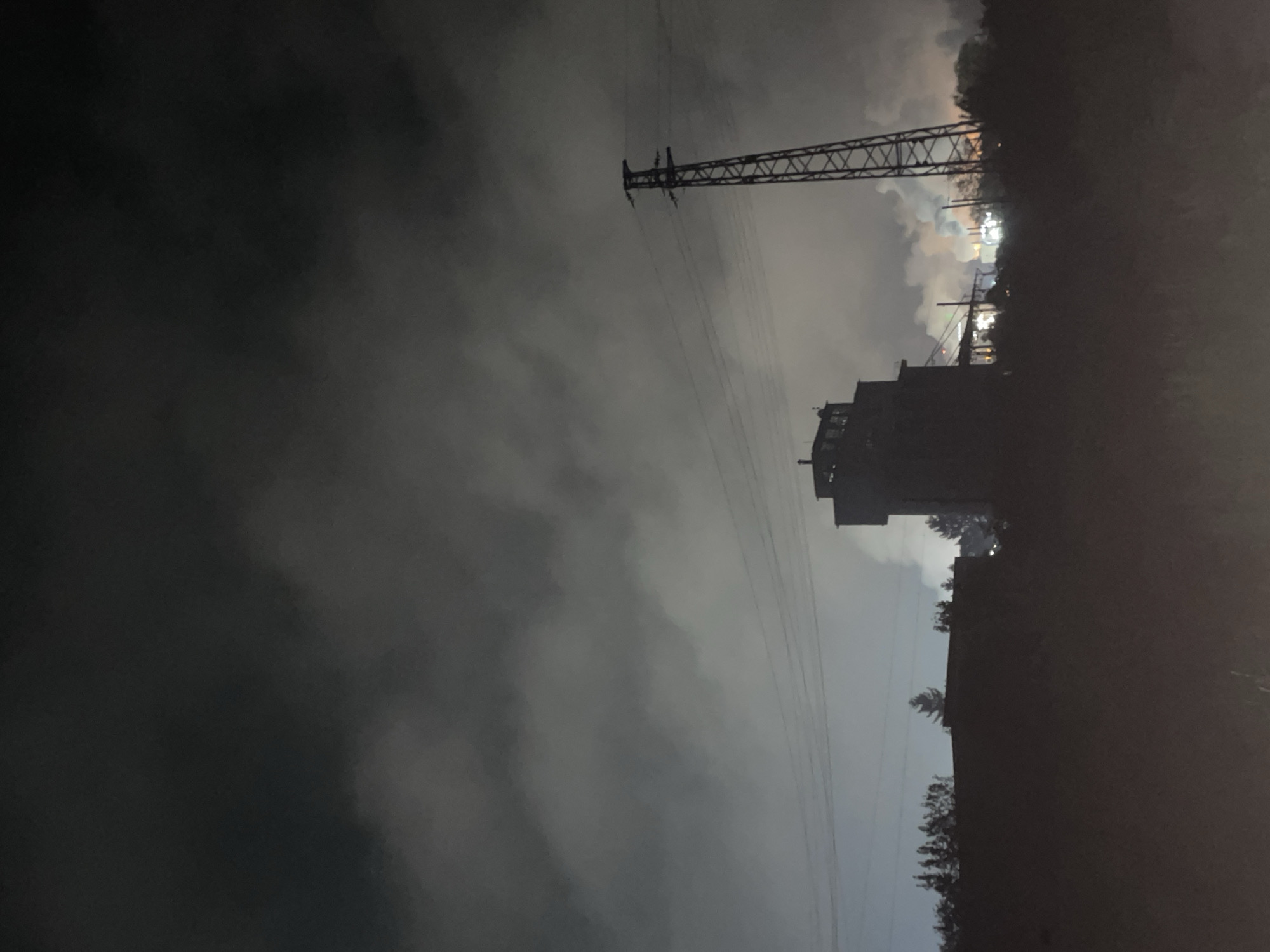 The image shows an industrial area at night with a large building and a transmission tower. The sky is cloudy, and there are trees in the foreground. Based on the details visible, the location is in Razgrad, Bulgaria.