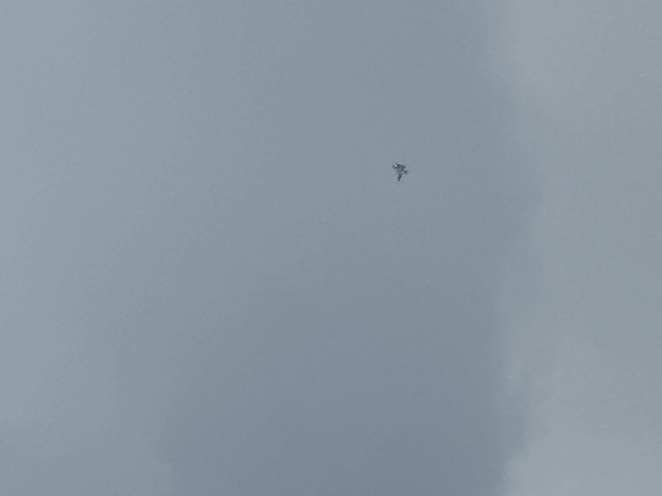 The image shows a small, gray aircraft flying in a gray sky with a few white clouds. The aircraft is flying high in the sky and appears to be a small, single-engine plane. The coordinates provided place the location in Krushynka, Ukraine, but the image does not depict any features of Krushynka, Ukraine.