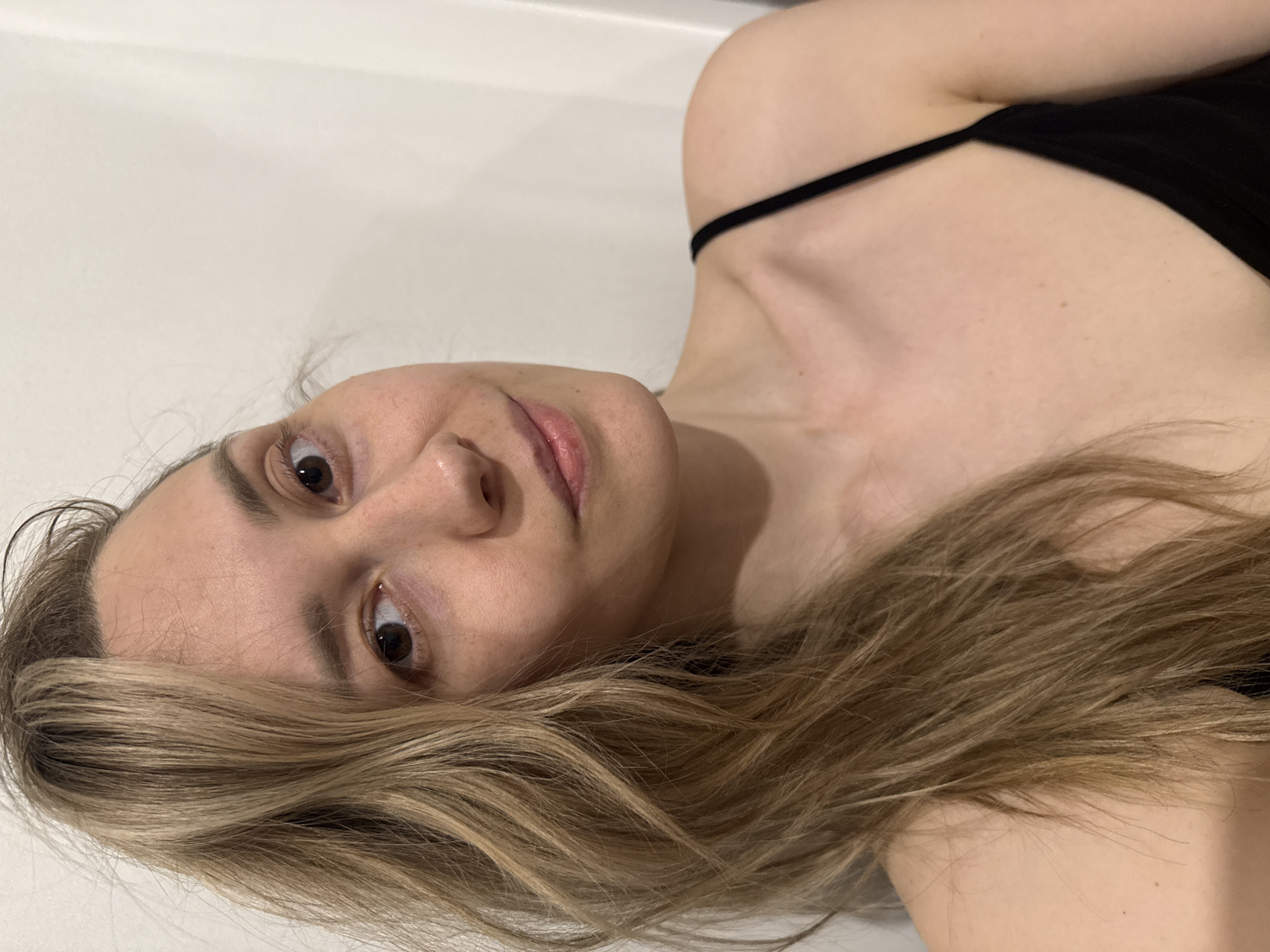 A blonde woman is lying on a white surface. She is wearing a black top with spaghetti straps. The location and details about the city of Chaikovsky, Russia are not discernible from the image.