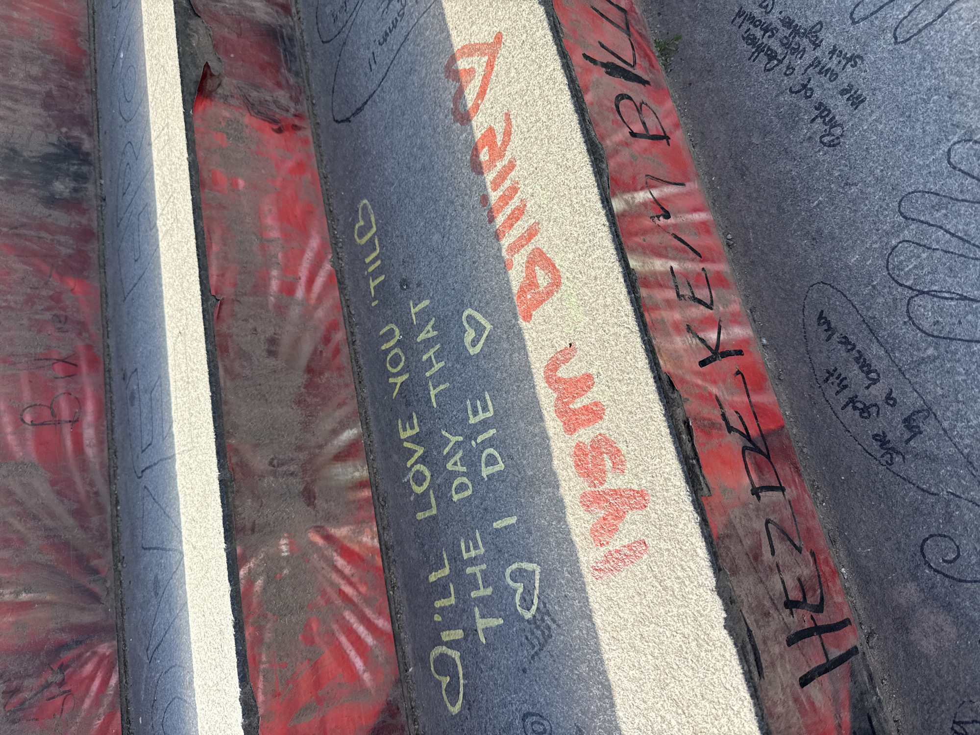 The image shows a close-up of painted inscriptions on the steps of a pedestrian walkway, likely located in Berlin, Germany. The steps are a combination of painted surfaces, with some areas appearing weathered and worn. The painted surfaces consist of red, white, and grey. The inscriptions include phrases like "I'LL LOVE YOU 'TILB THE DAY THAT ♡ I DIE ♡", "lysm Billie", "HEZDEKE/MBK", and "She got hit by a baraka". There is also a phrase "Birds of a feather lid stick together". The inscriptions are written in varying styles and colors, suggesting different authors. The steps appear to be heavily used.