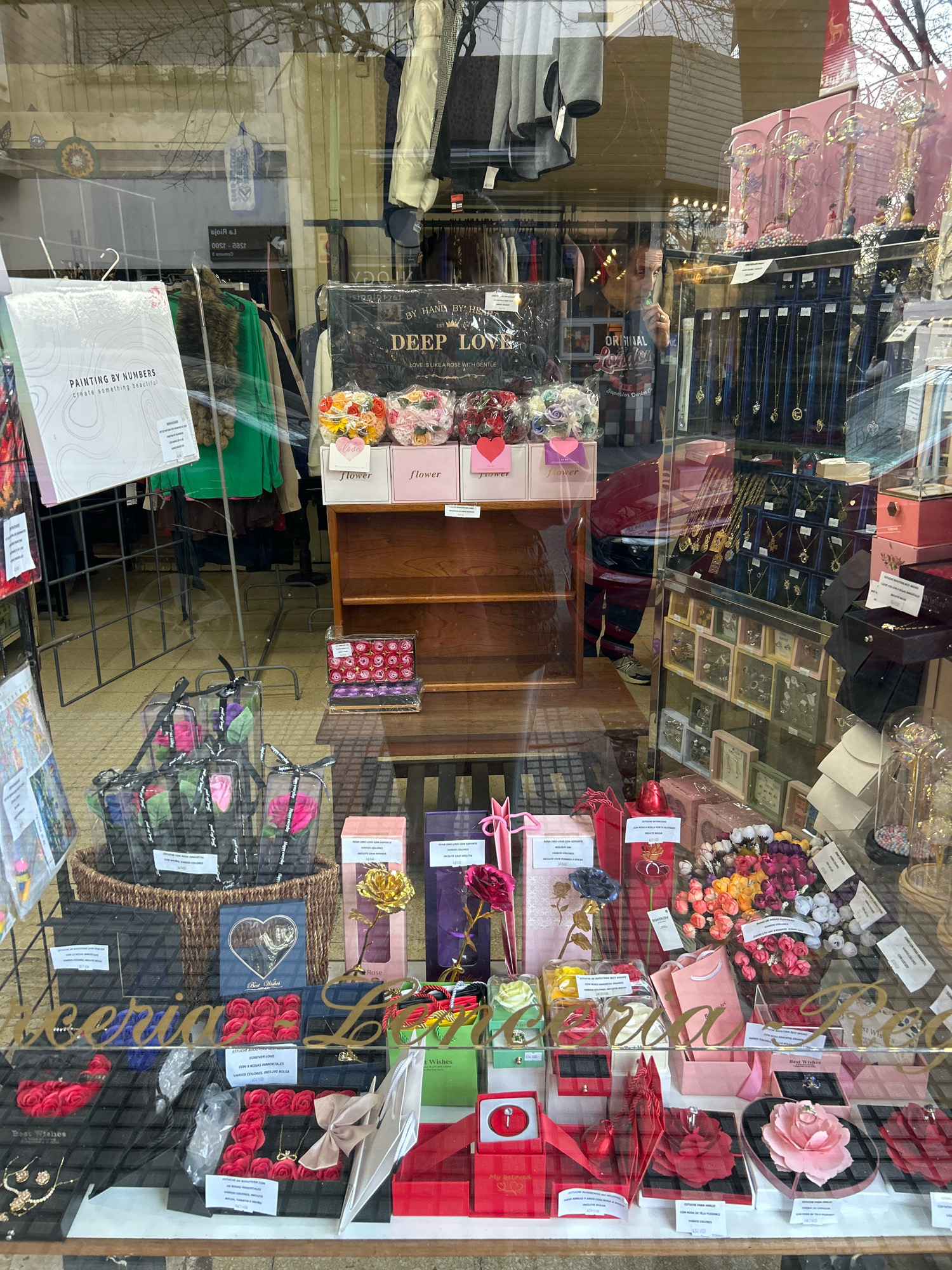 The image shows a storefront display of a gift shop in Buenos Aires, Argentina. The display is filled with various items, including artificial flowers, jewelry, gift boxes, and decorative items. The storefront appears to be made of glass, allowing a view of the merchandise inside. The items are arranged in a visually appealing manner, with a focus on romantic and celebratory themes. There are some reflections visible on the glass, indicating the presence of an outdoor environment. The overall impression is that of a well-stocked and inviting gift shop.