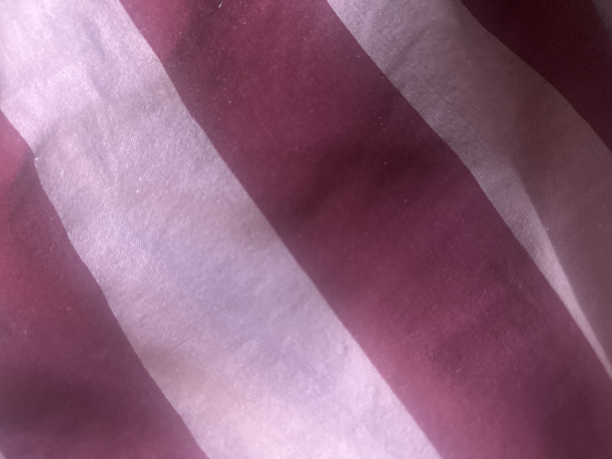 The image shows a close-up view of striped fabric, with alternating bands of dark pink and lighter pink or white. The fabric appears to be slightly wrinkled and has a textured appearance. The lighting suggests it is an indoor setting. There are no discernible features that would allow for the determination of a specific location within Thora, Australia, or any details about people, actions, or interactions.